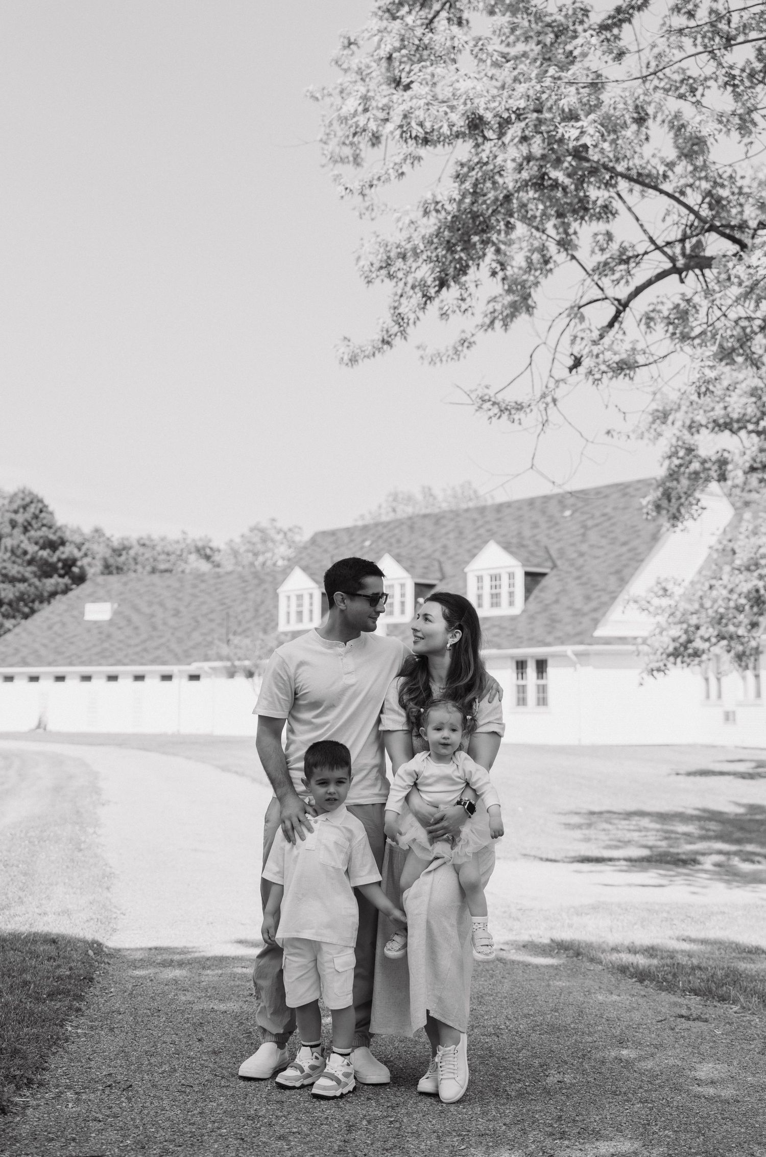 Black and white portrait of a family standing together on a lawn with a white house in the background.