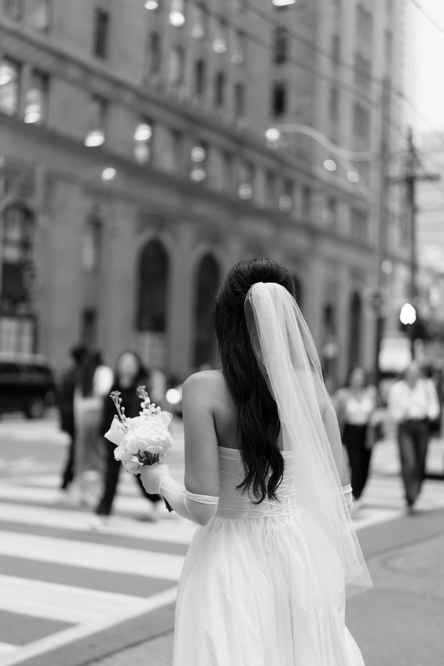 A bride in a white wedding dress and veil walks down a Toronto street in black and white photography.  in Toronto by AZ Photo Studio.