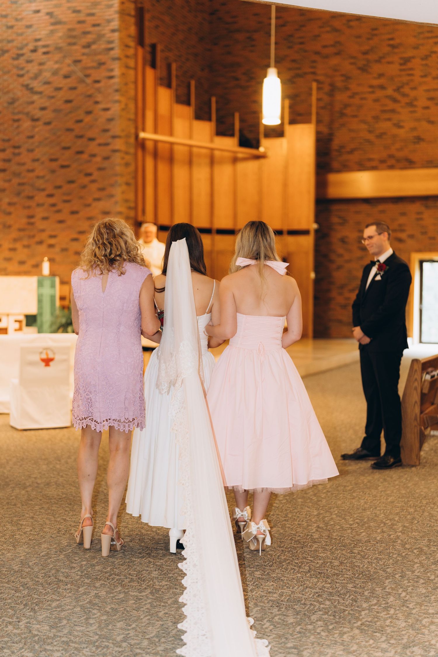 A group in white attire walks through a modern corridor with brick walls and pendant lighting.