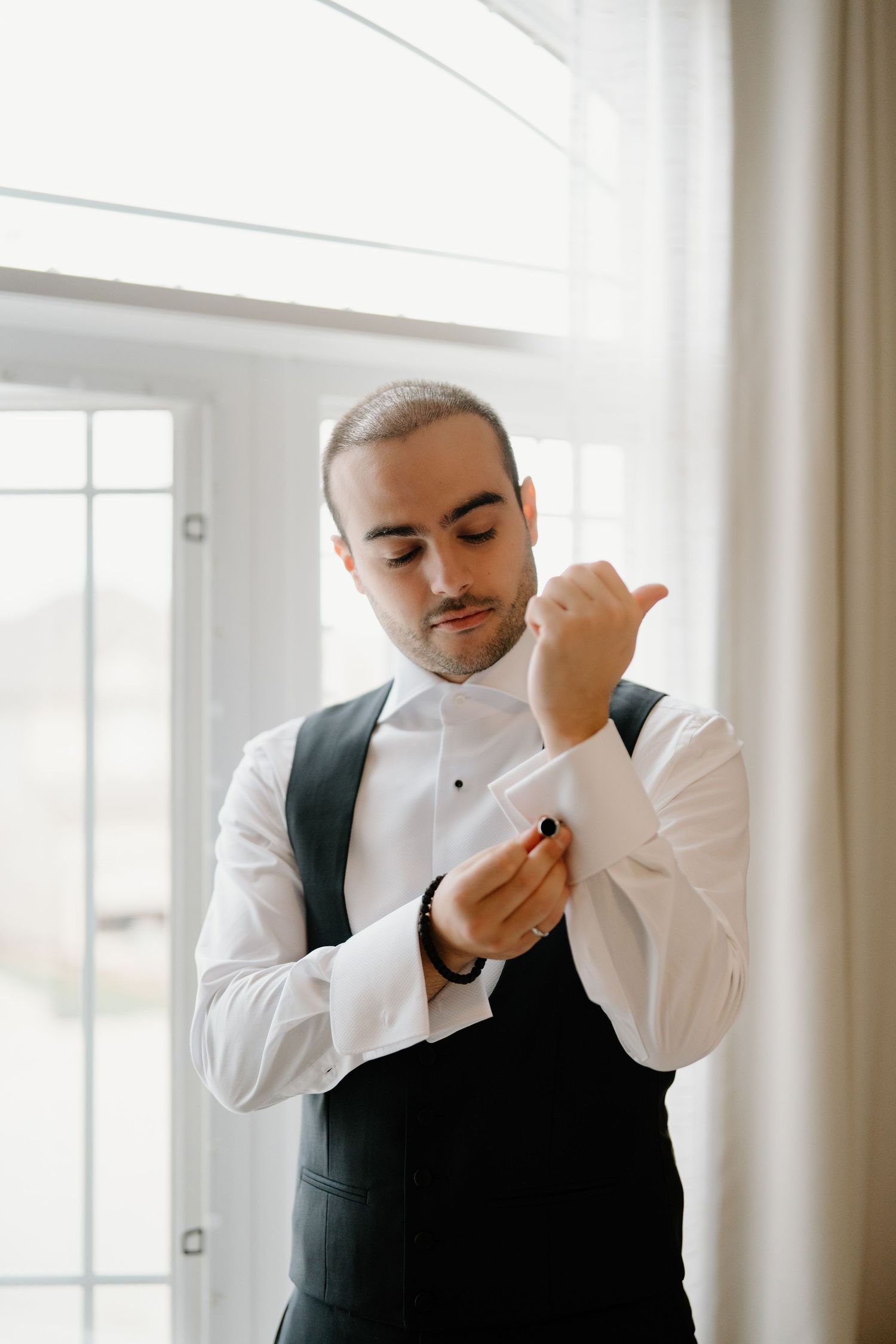 A person in a black vest and white shirt dabs their nose with a white tissue in a bright interior space.