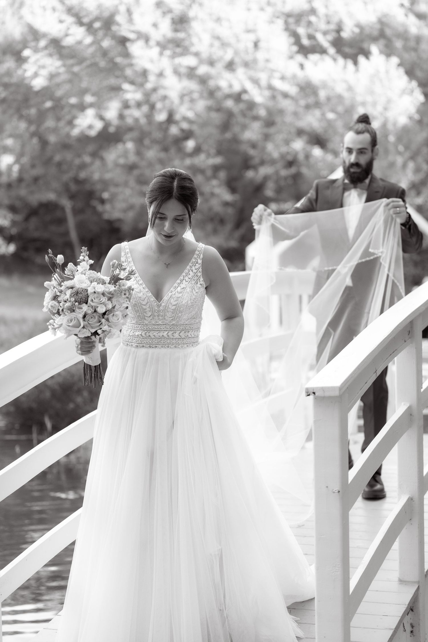 Black and white photo of bride in flowing dress descending white bridge steps with veil.