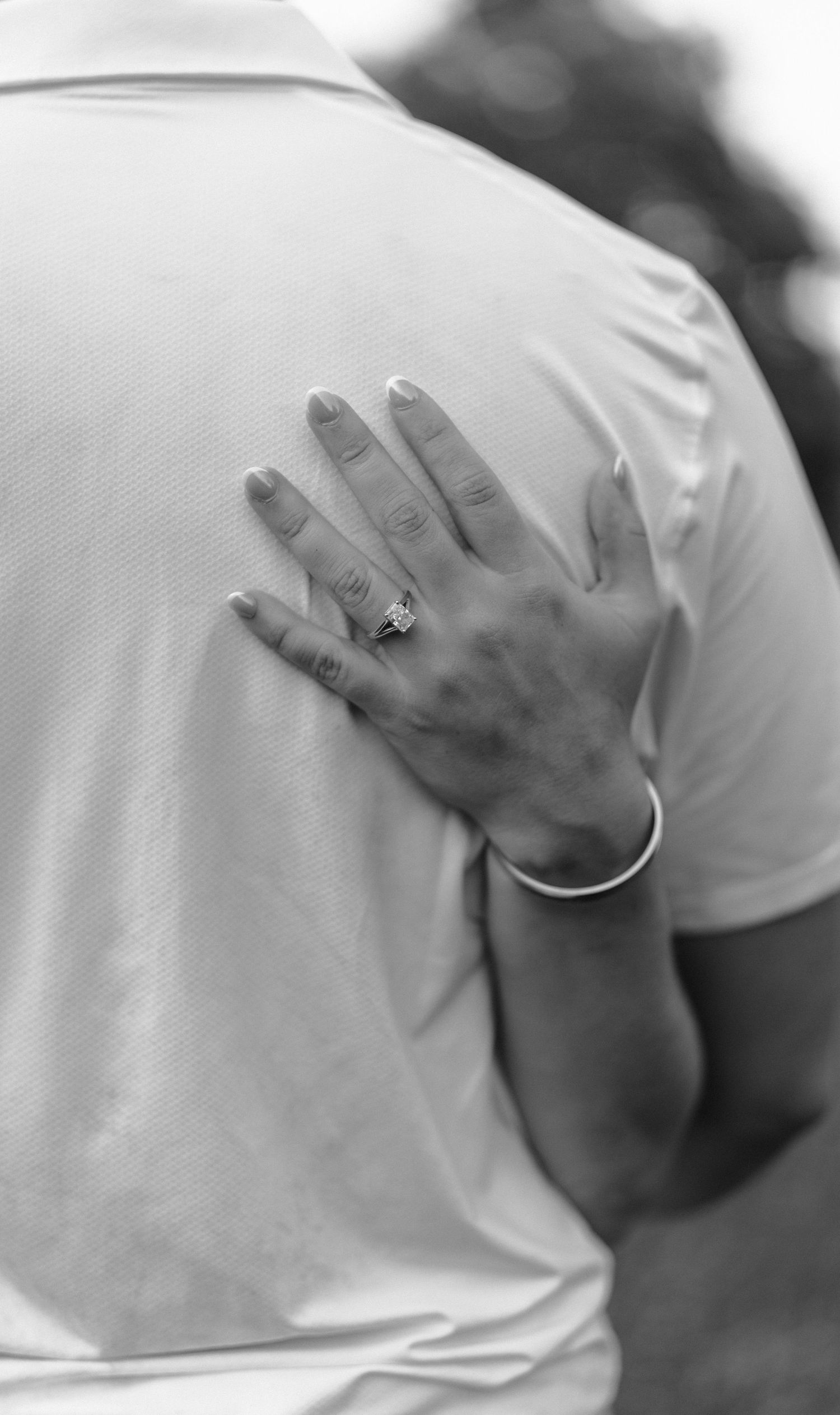 Close-up black and white photograph of hands with wedding rings against a white fabric background.