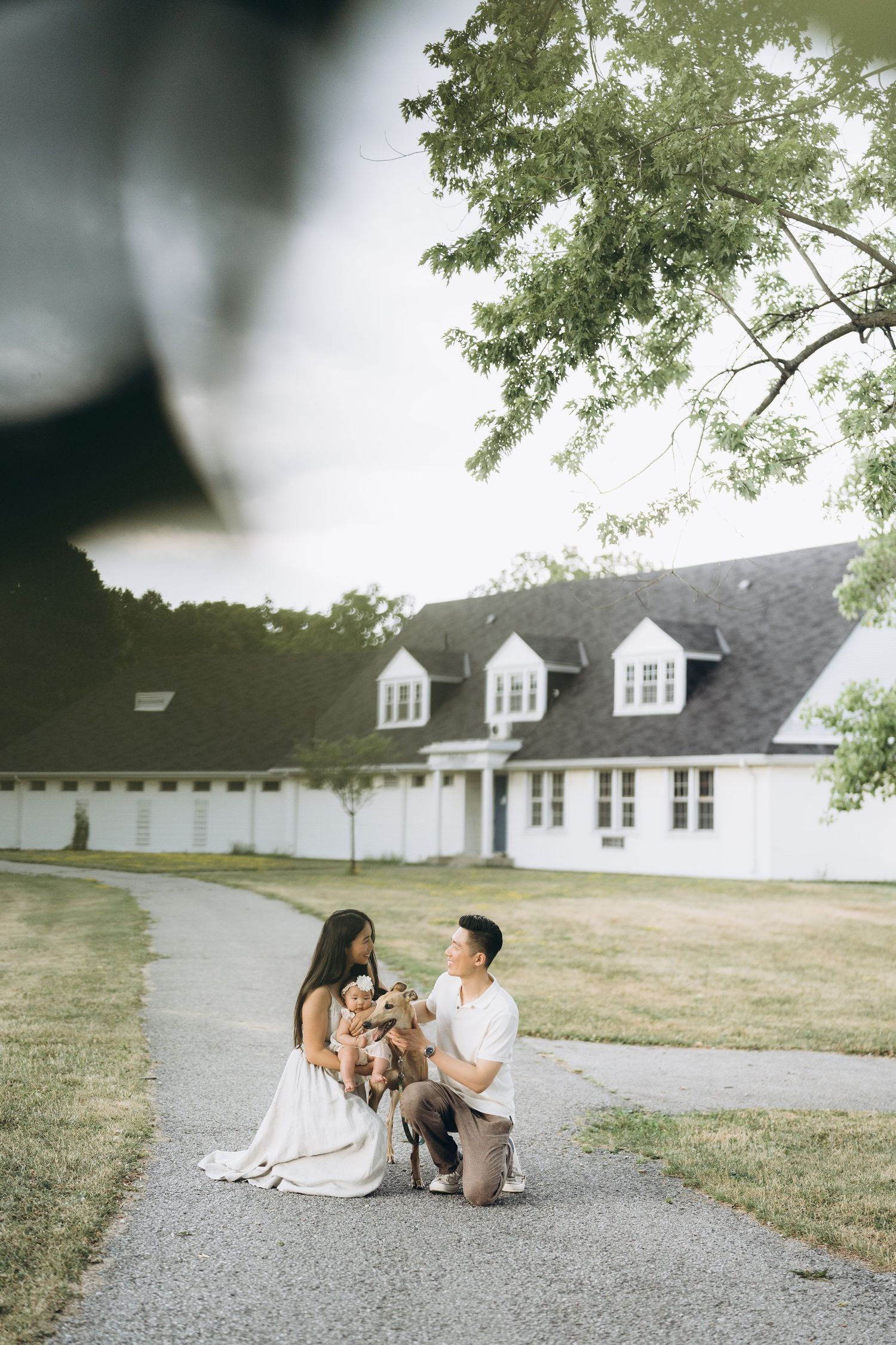 A couple sits with their dog on a pathway in front of a classic white colonial building.