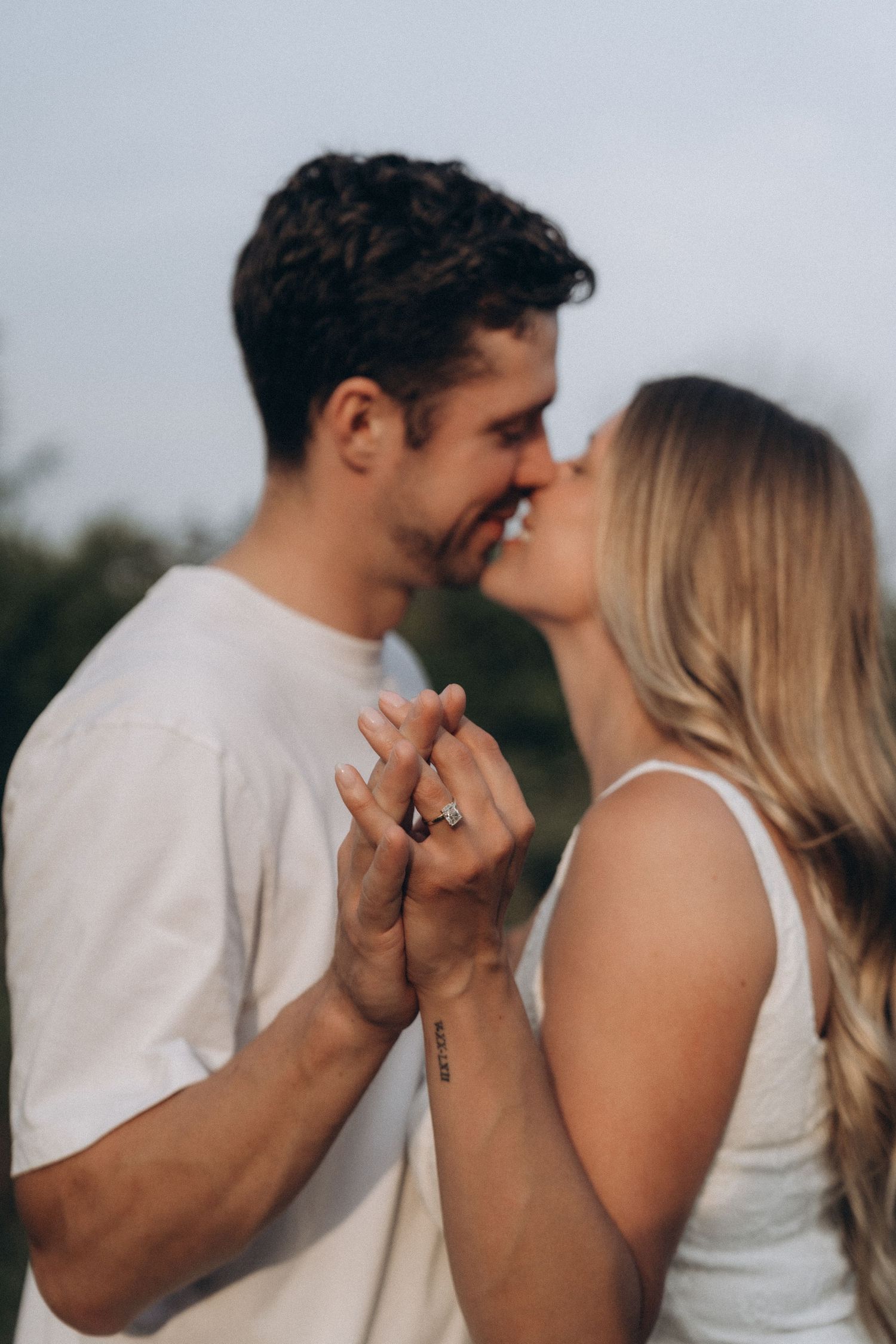 Romantic couple in white outfits holding hands and sharing an intimate moment outdoors.