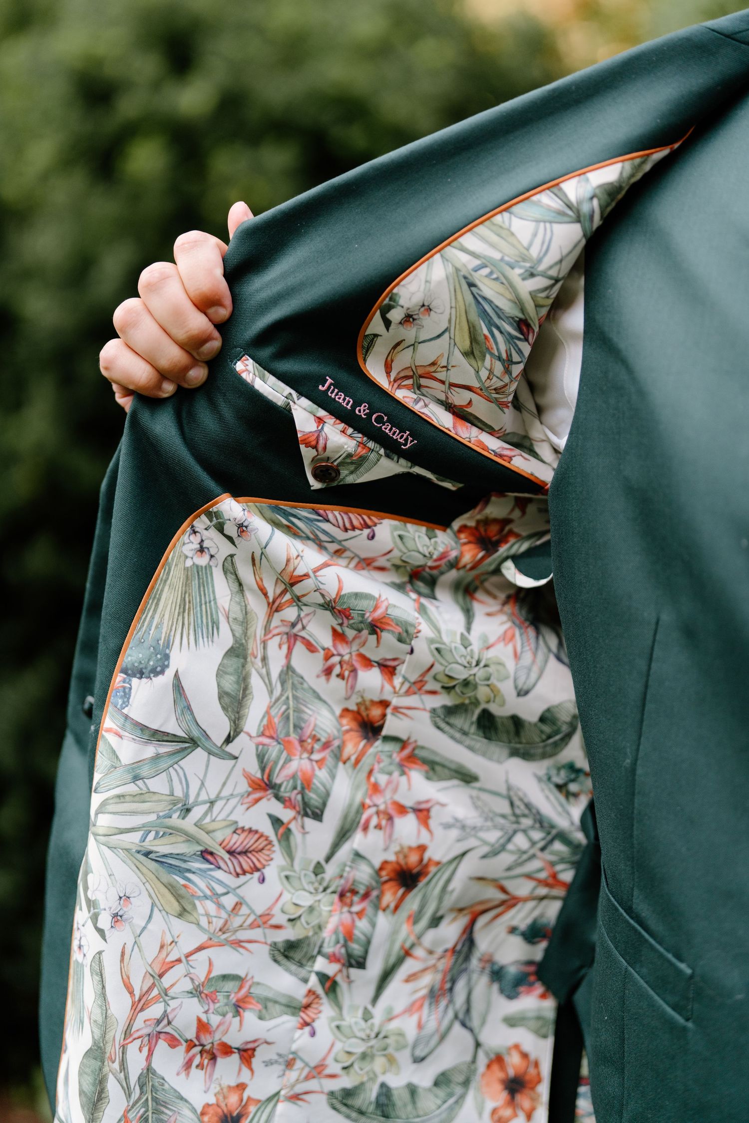 Close-up view of a dark green jacket being opened to reveal a floral patterned lining with birds and botanical designs.
