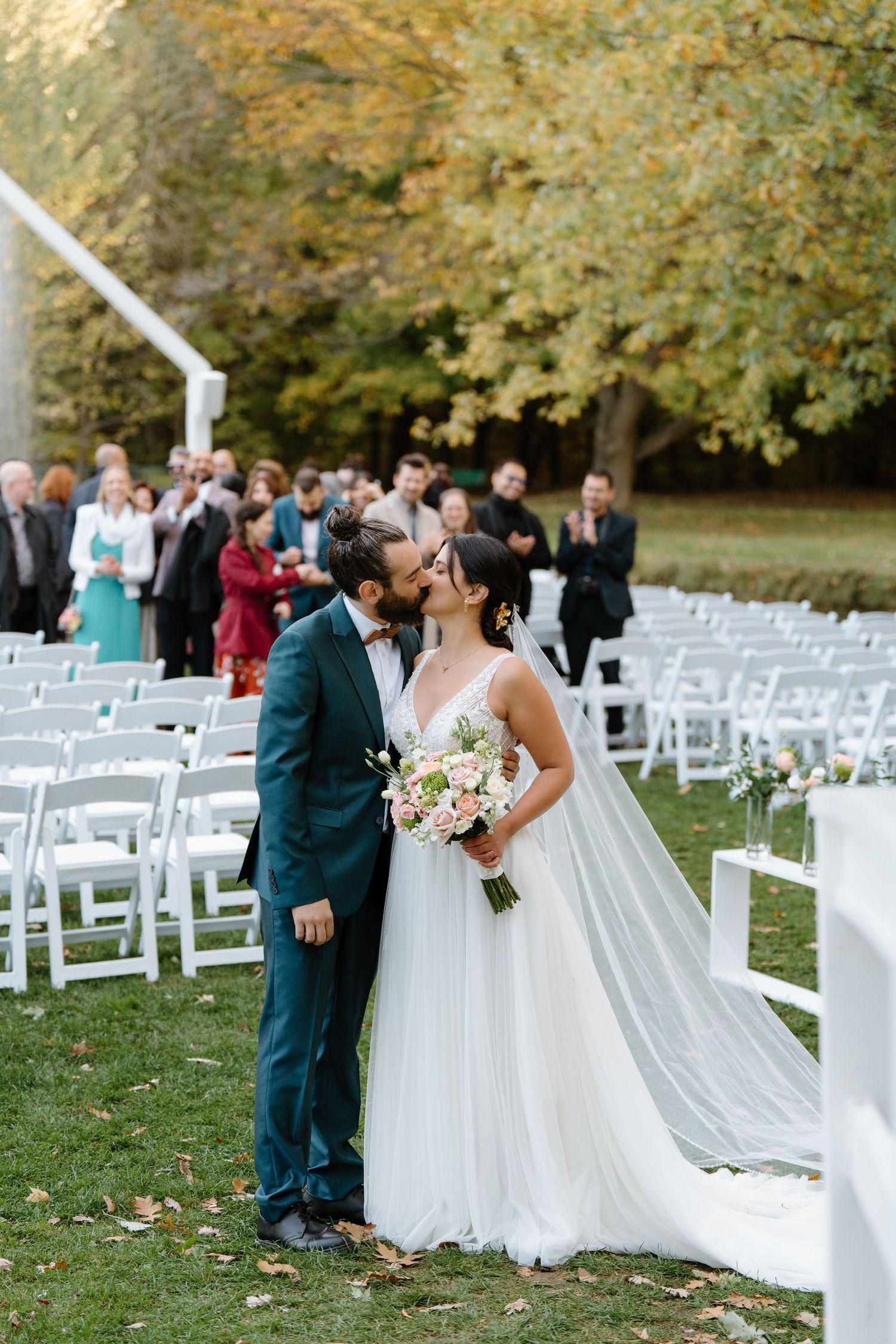 Outdoor fall wedding with couple sharing intimate moment among white chairs and autumn foliage.
