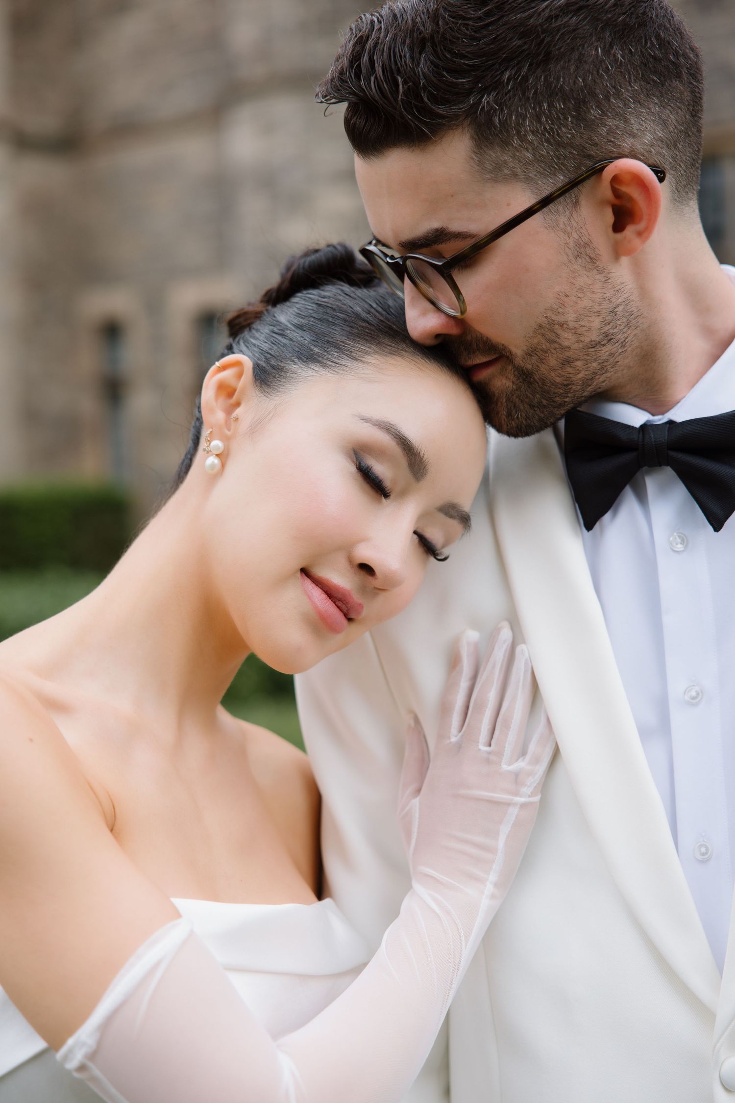 A romantic wedding portrait showing a couple in elegant white attire with the bride wearing long gloves and groom in a bowtie.