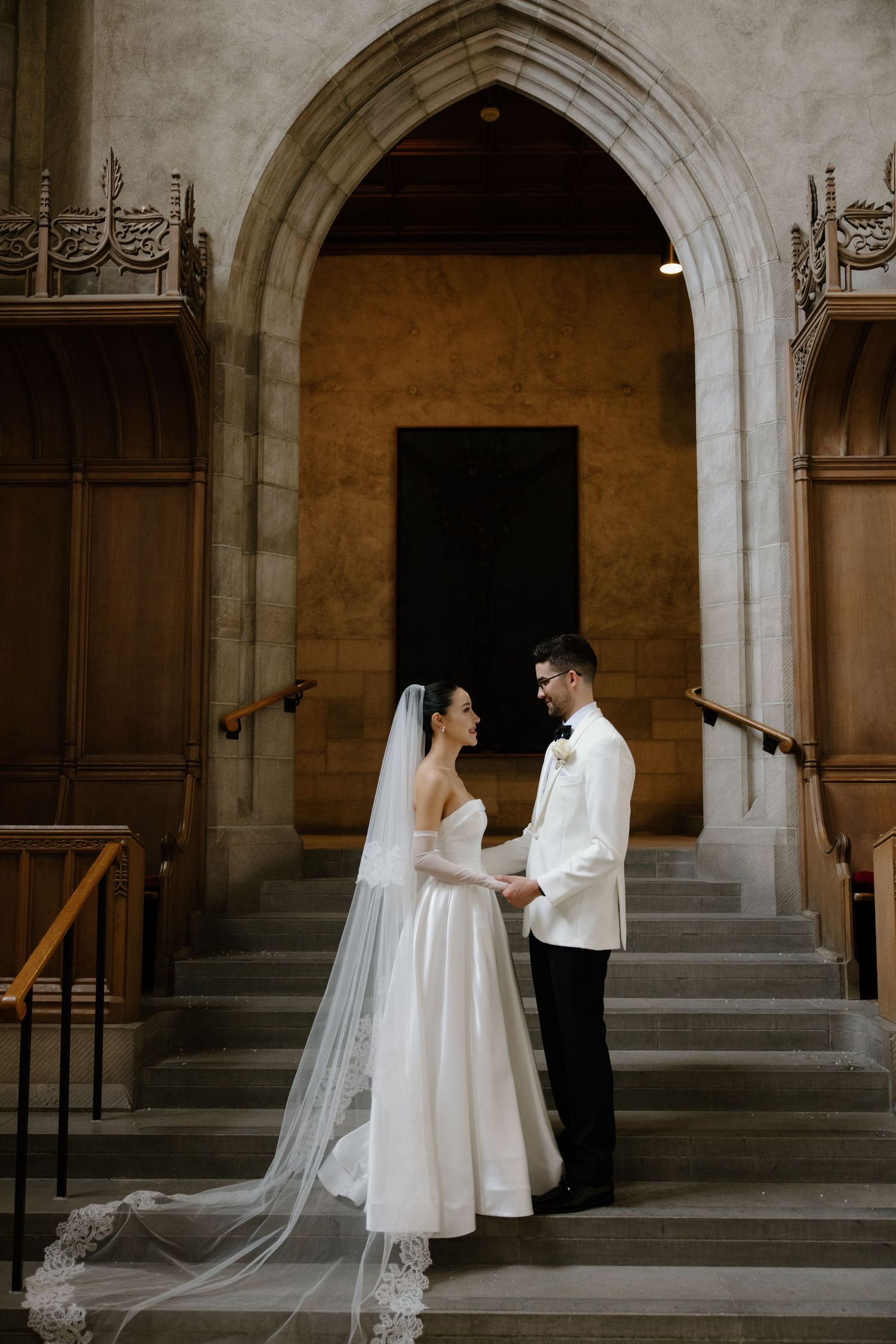 Bride and groom share a traditional first look moment under stone archways in a historic building.
