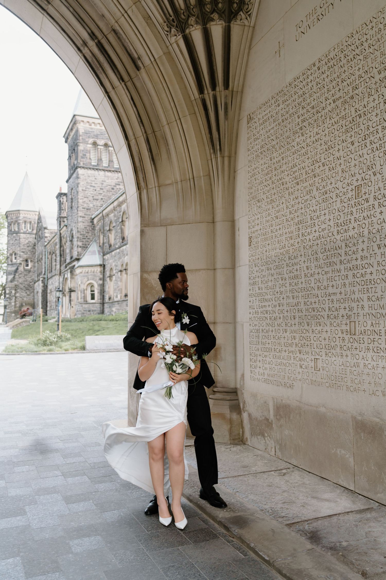 A romantic moment captured under a stone archway with ornate writing carved into its walls.