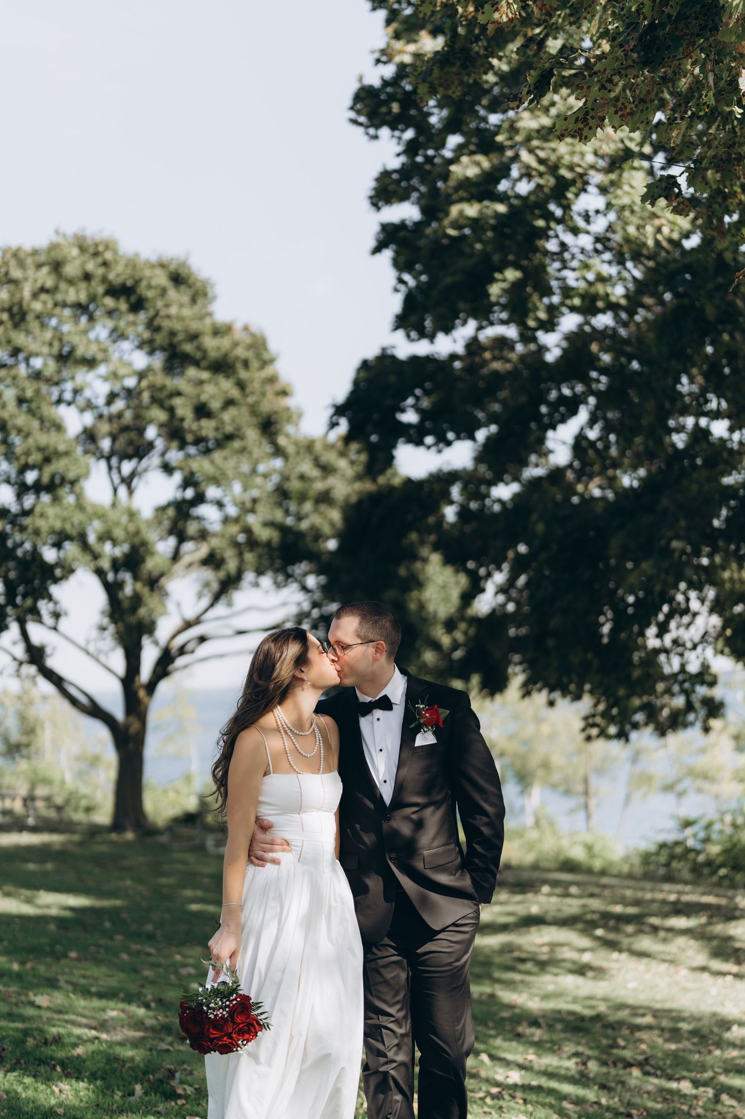 Four separate shots of a romantic outdoor wedding scene with a couple kissing among tall trees on a grassy hill.