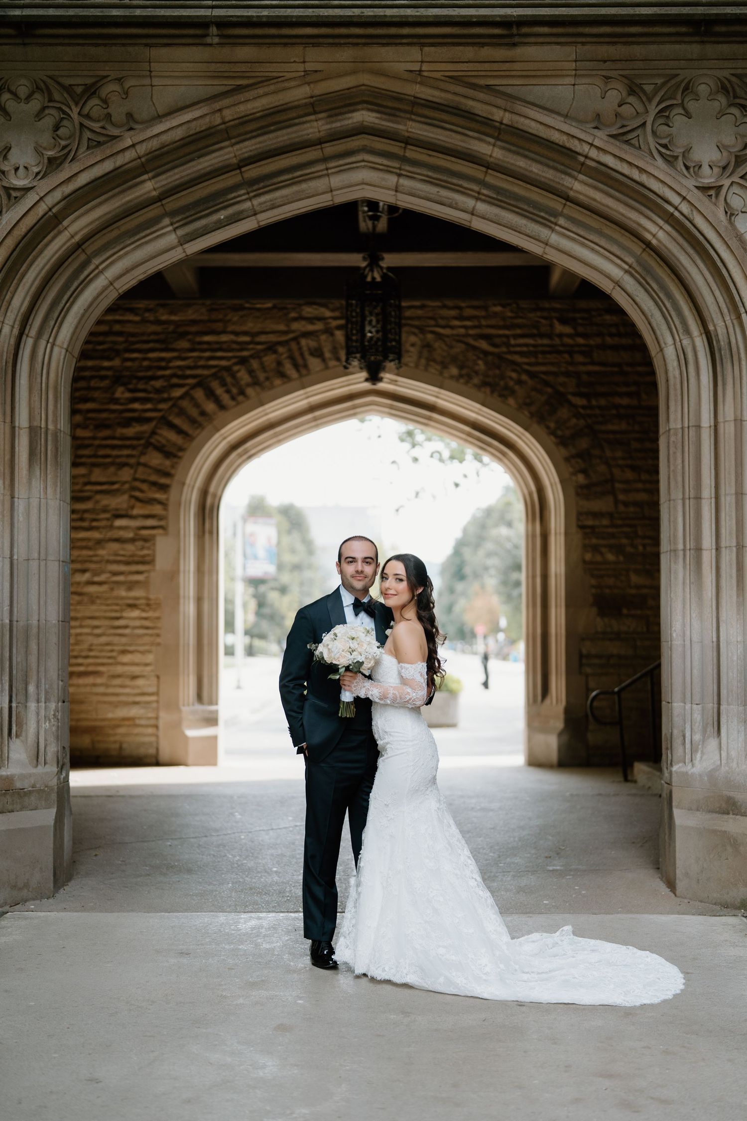A bride and groom share a romantic moment under gothic stone arches at their wedding.