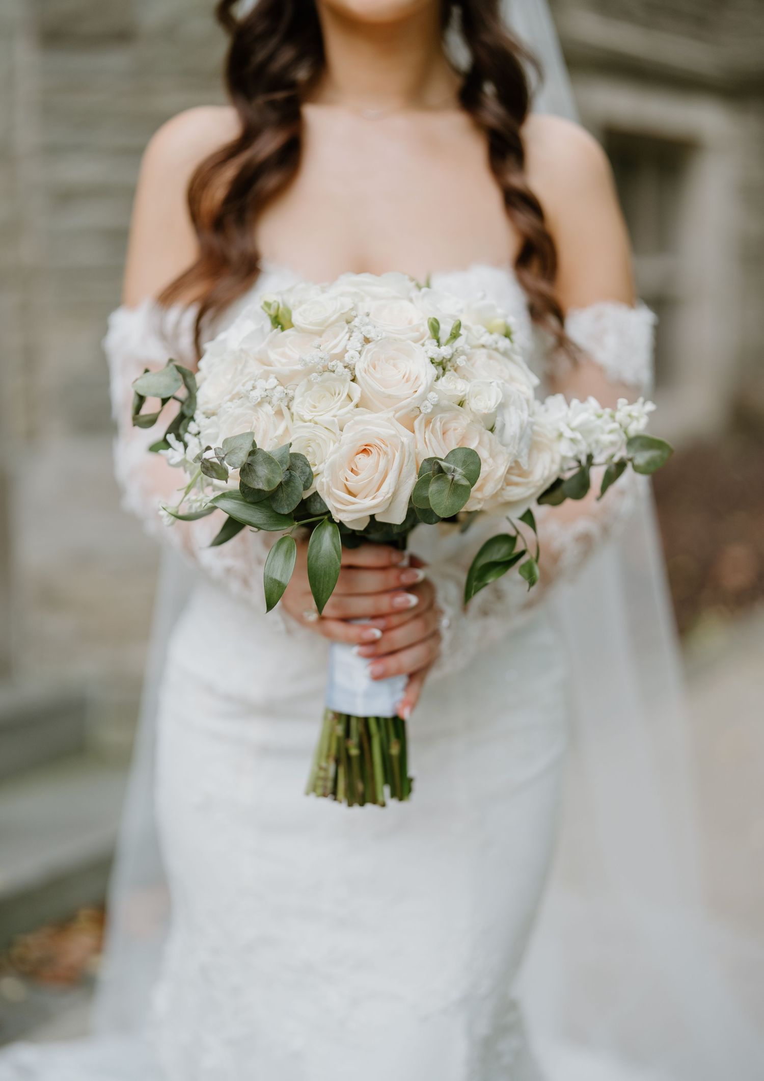 Elegant white bridal bouquet featuring soft roses and eucalyptus greenery held against a lace wedding dress.