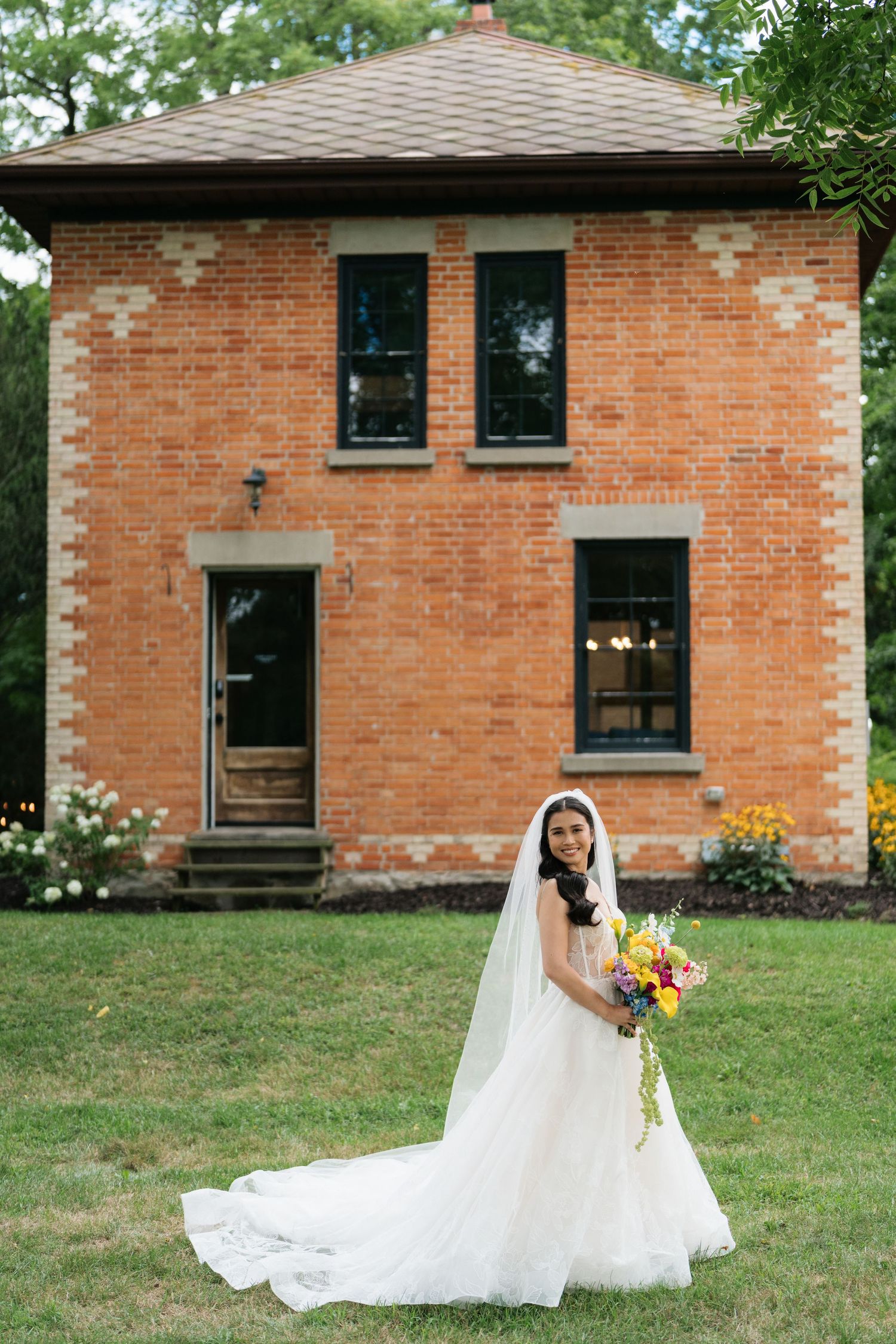 A beautiful wedding scene with a flowing white dress and sunflowers against a rustic brick building backdrop.