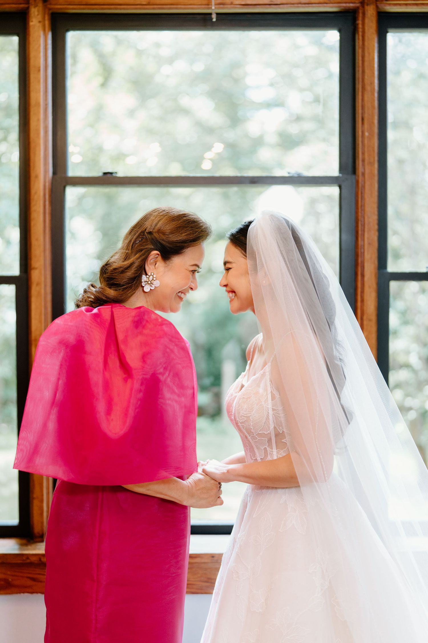 A touching moment shared between two people in formal attire, one wearing a bright pink dress and one in a white gown.