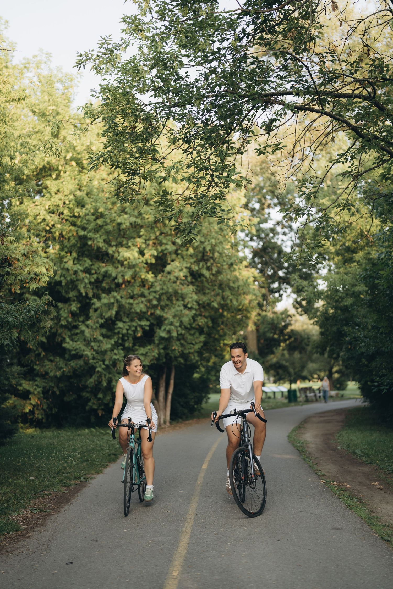 Cyclists riding bikes along a shaded tree-lined path during a sunny afternoon in the park.