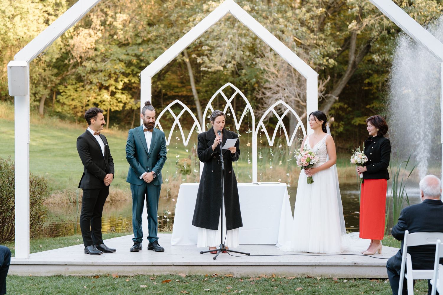 Wedding ceremony under white geometric arch structure in garden setting.