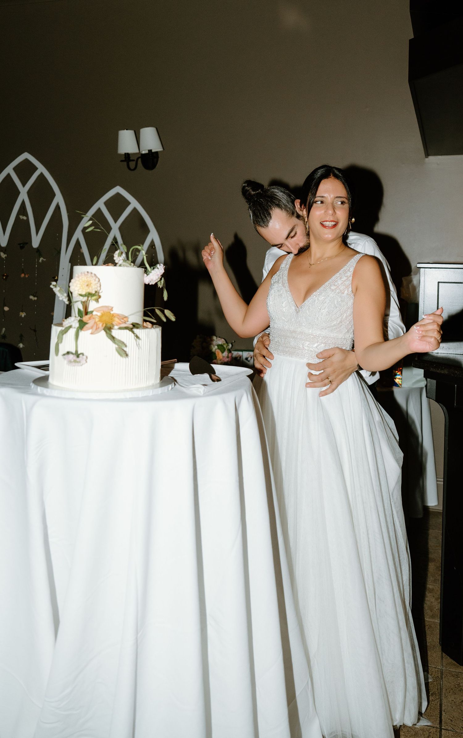 Newlyweds share a joyful moment while cutting their elegant white wedding cake.