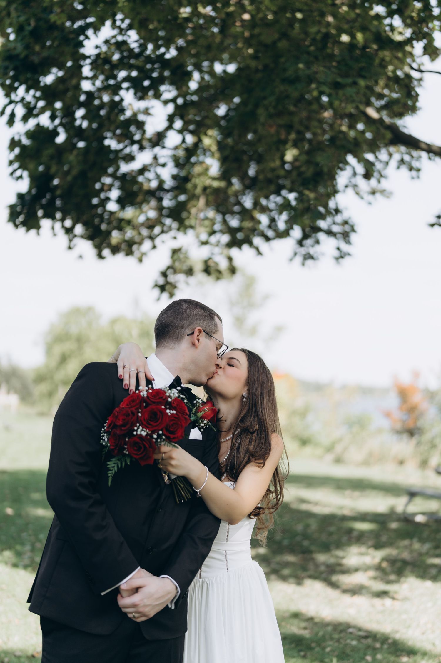 A romantic couple shares intimate kisses in an outdoor garden setting wearing formal wedding attire.