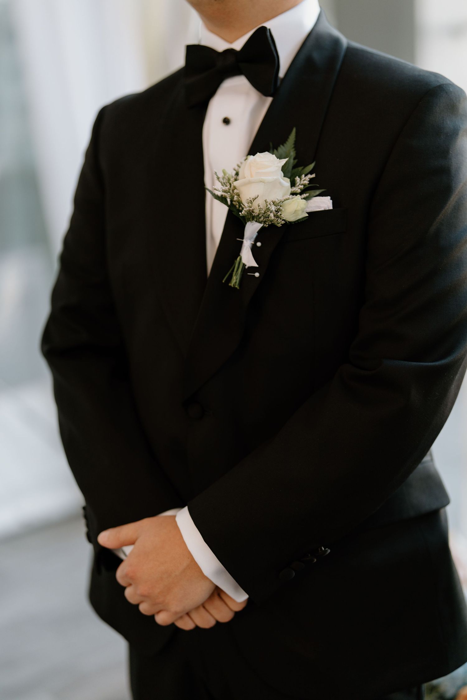 Close-up of groom in classic black tuxedo with white boutonniere and bow tie on wedding day.