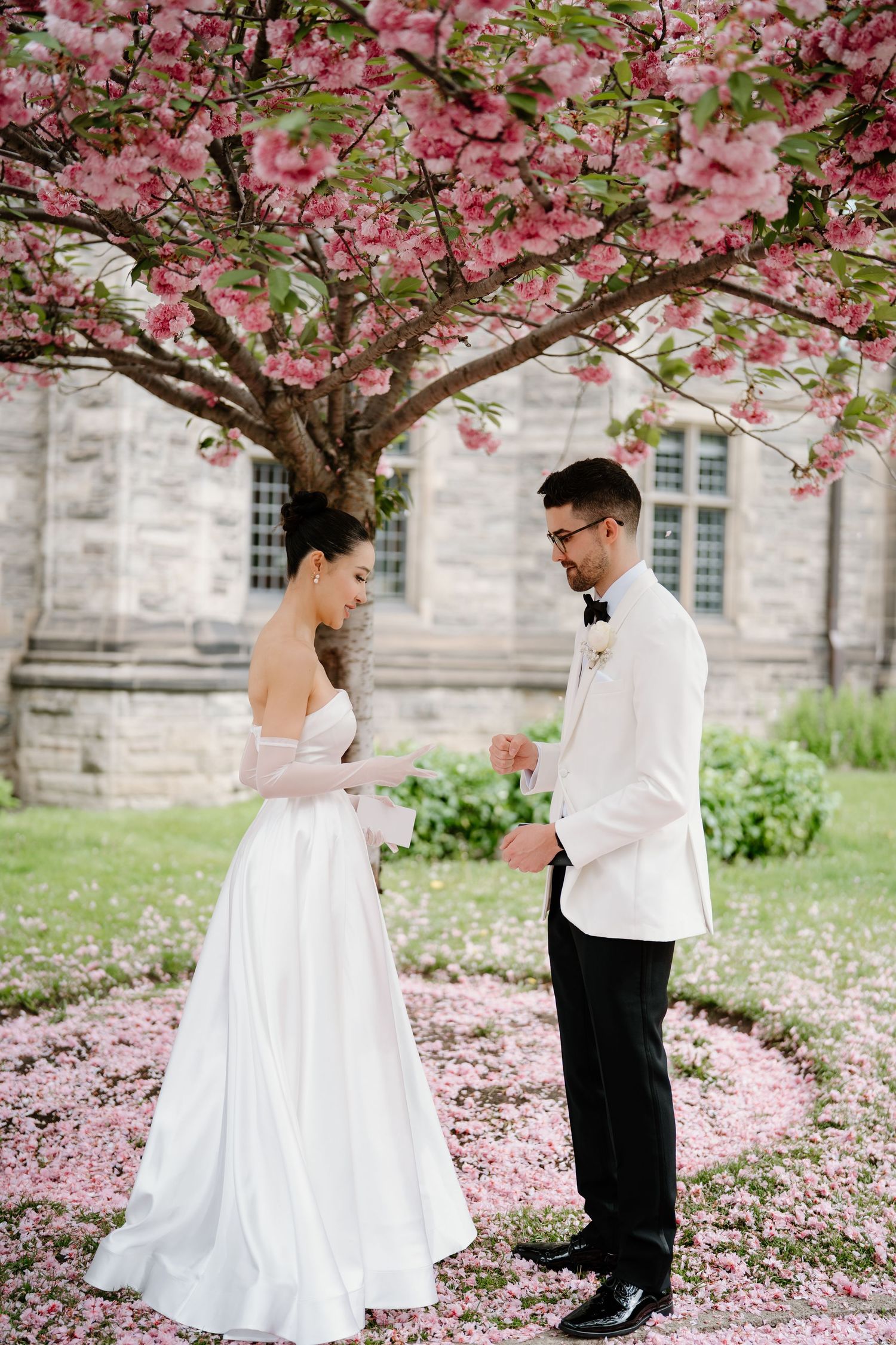 Couple shares an intimate first look beneath a flowering cherry tree with delicate pink blossoms.