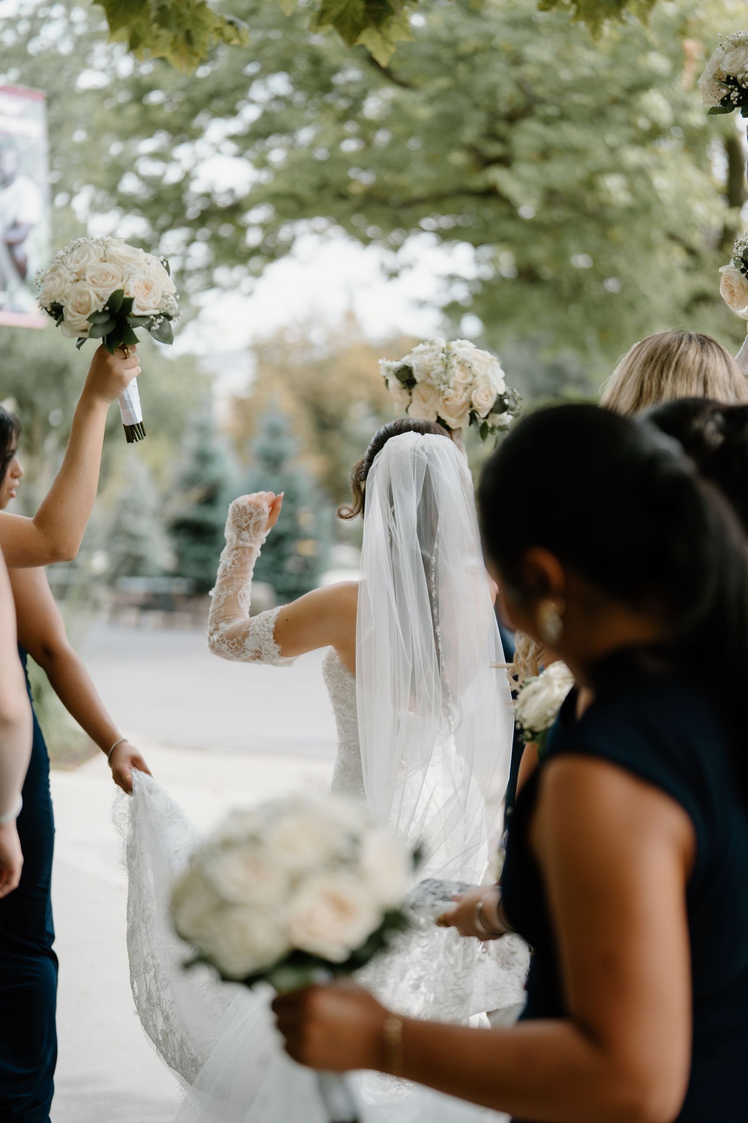 A group of wedding attendees throw white flower petals in celebration during an outdoor ceremony.