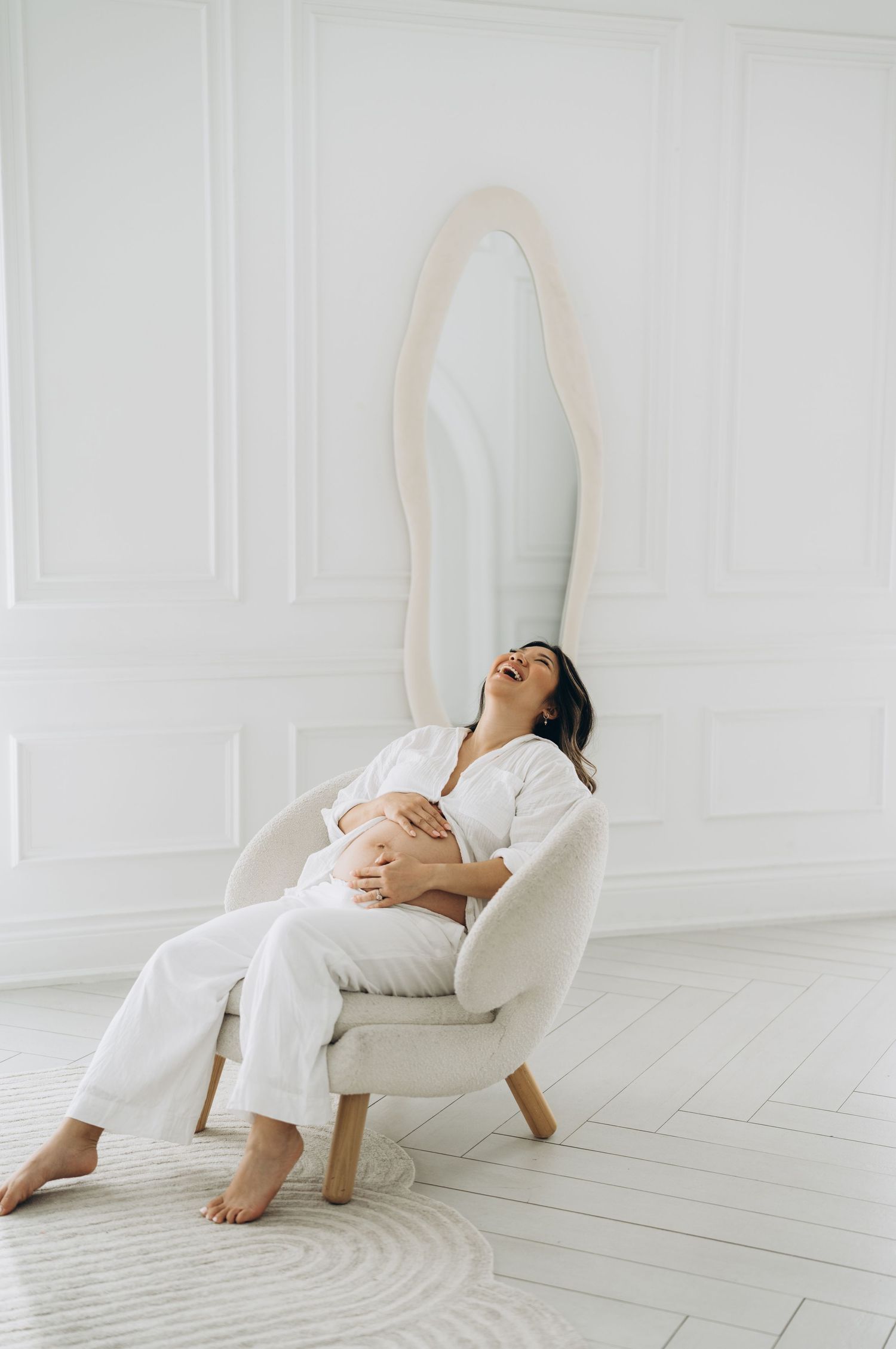 A person in white clothing rests peacefully in a modern white armchair against a minimalist white wall.