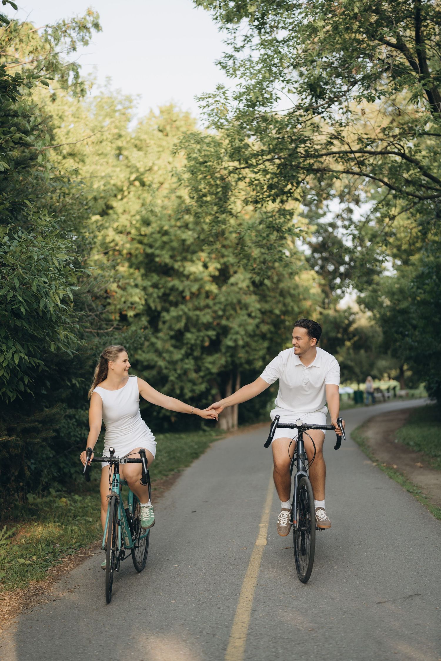 Happy couple cycling together on a tree-lined path during a summer evening.