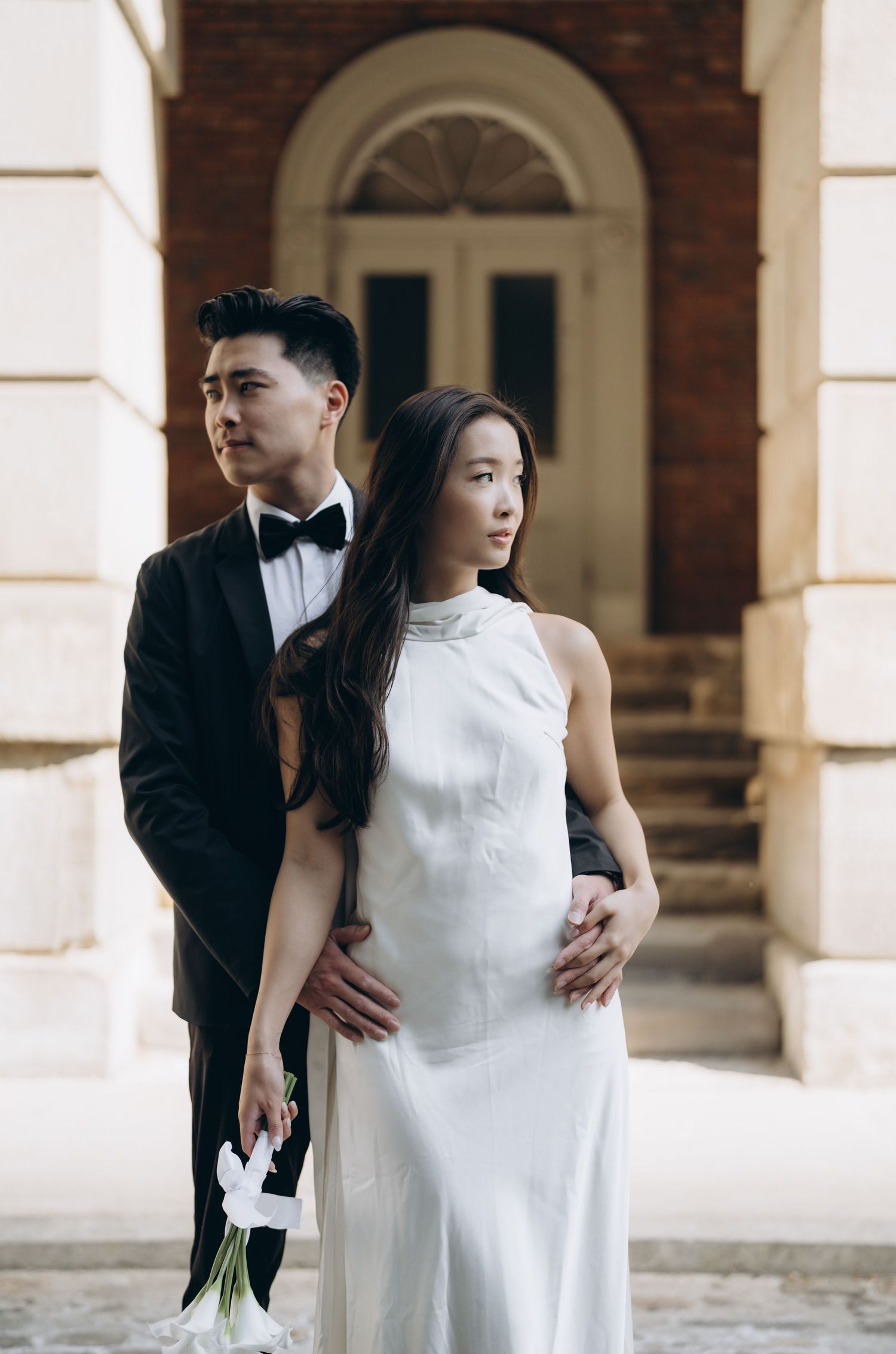 A couple in formal attire poses for an elegant portrait in front of an arched doorway at a historic building.
