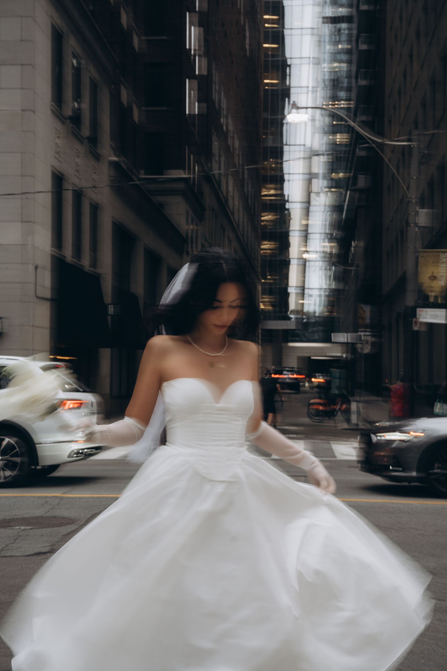A bride in a flowing white wedding dress twirls gracefully on a city street creating an ethereal motion blur effect.