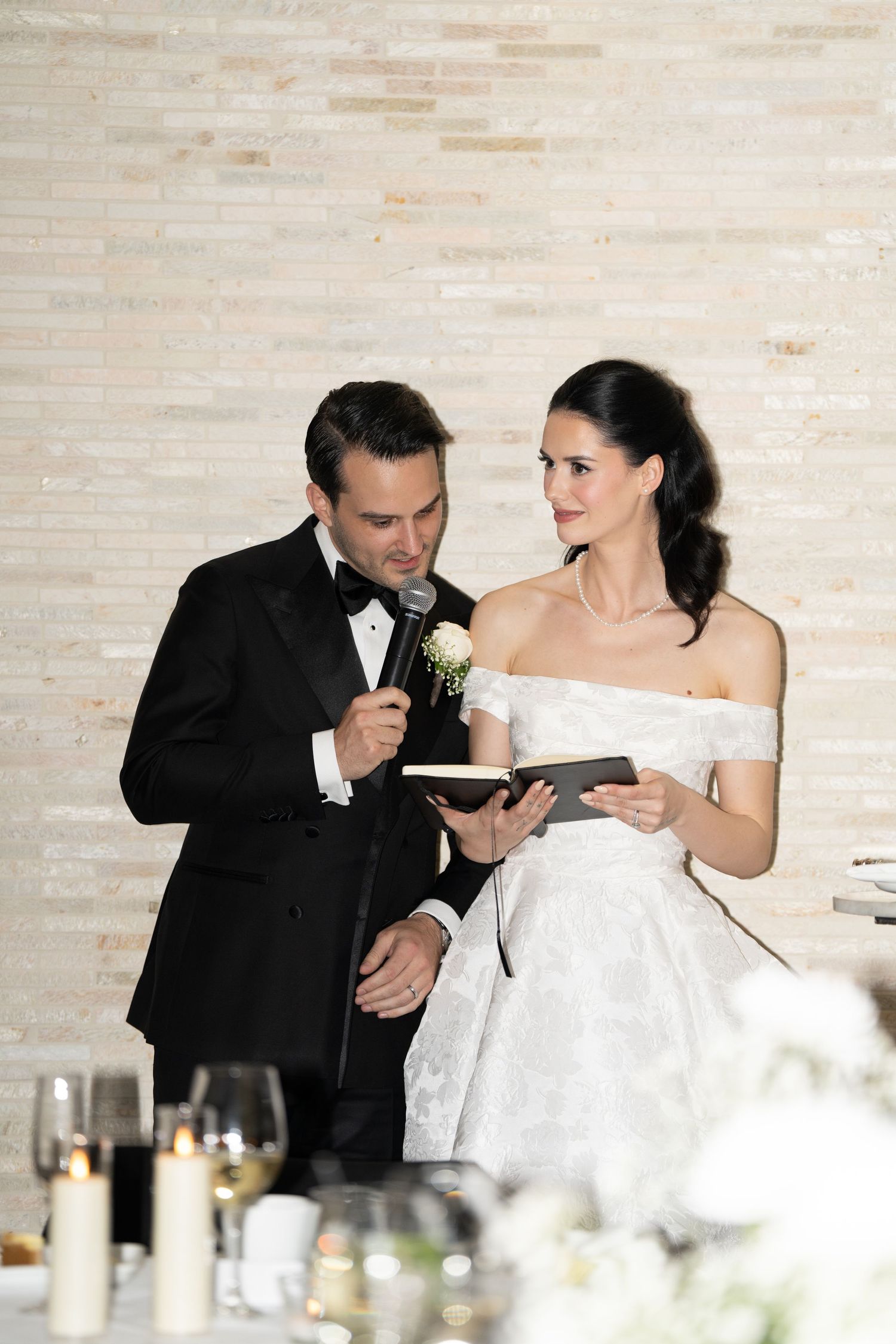 A couple in formal wedding attire share a moment while looking at a book or document during their reception.