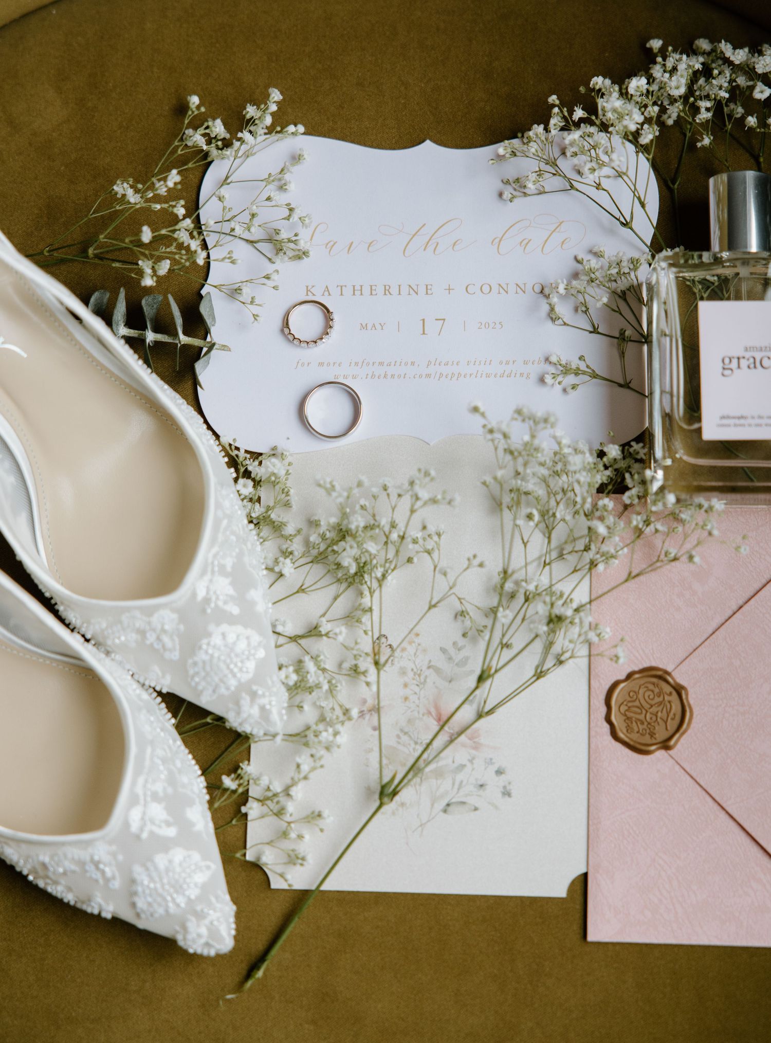 Flatlay of wedding accessories including baby's breath flowers, white shoes, rings, and invitation cards in neutral tones.