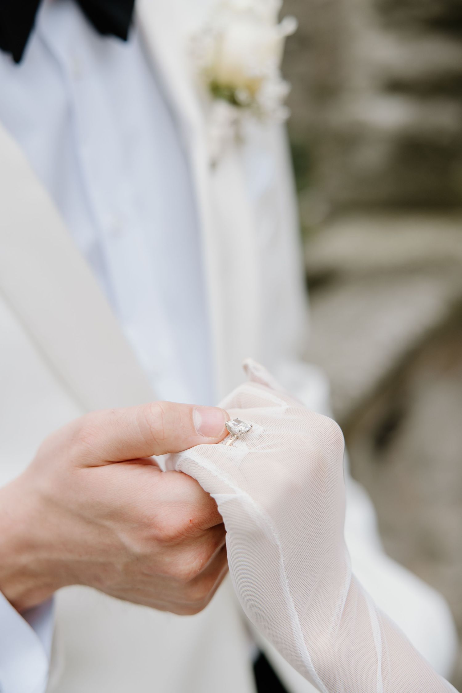 Close-up of hands delicately holding sheer white fabric against a light background.
