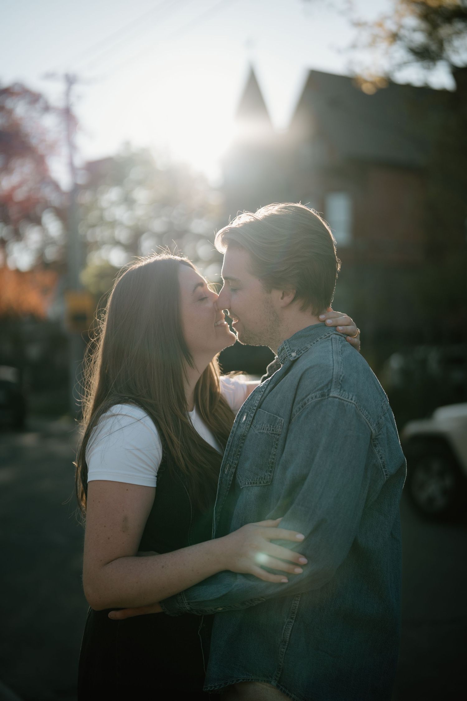 A romantic couple embraces in front of sun-lit house during golden hour on an autumn day.