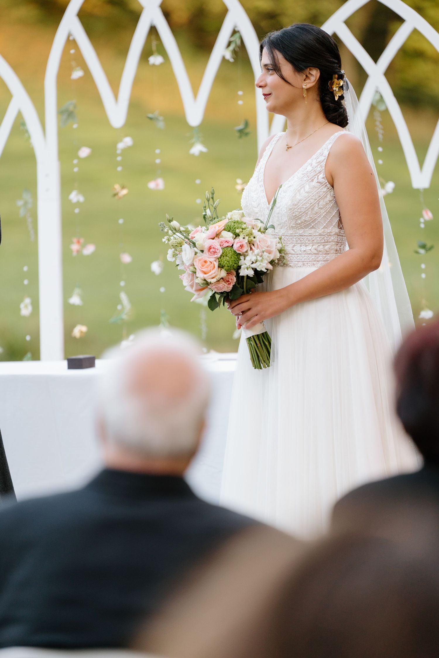 Outdoor wedding ceremony with white geometric arch and hanging crystal decorations.