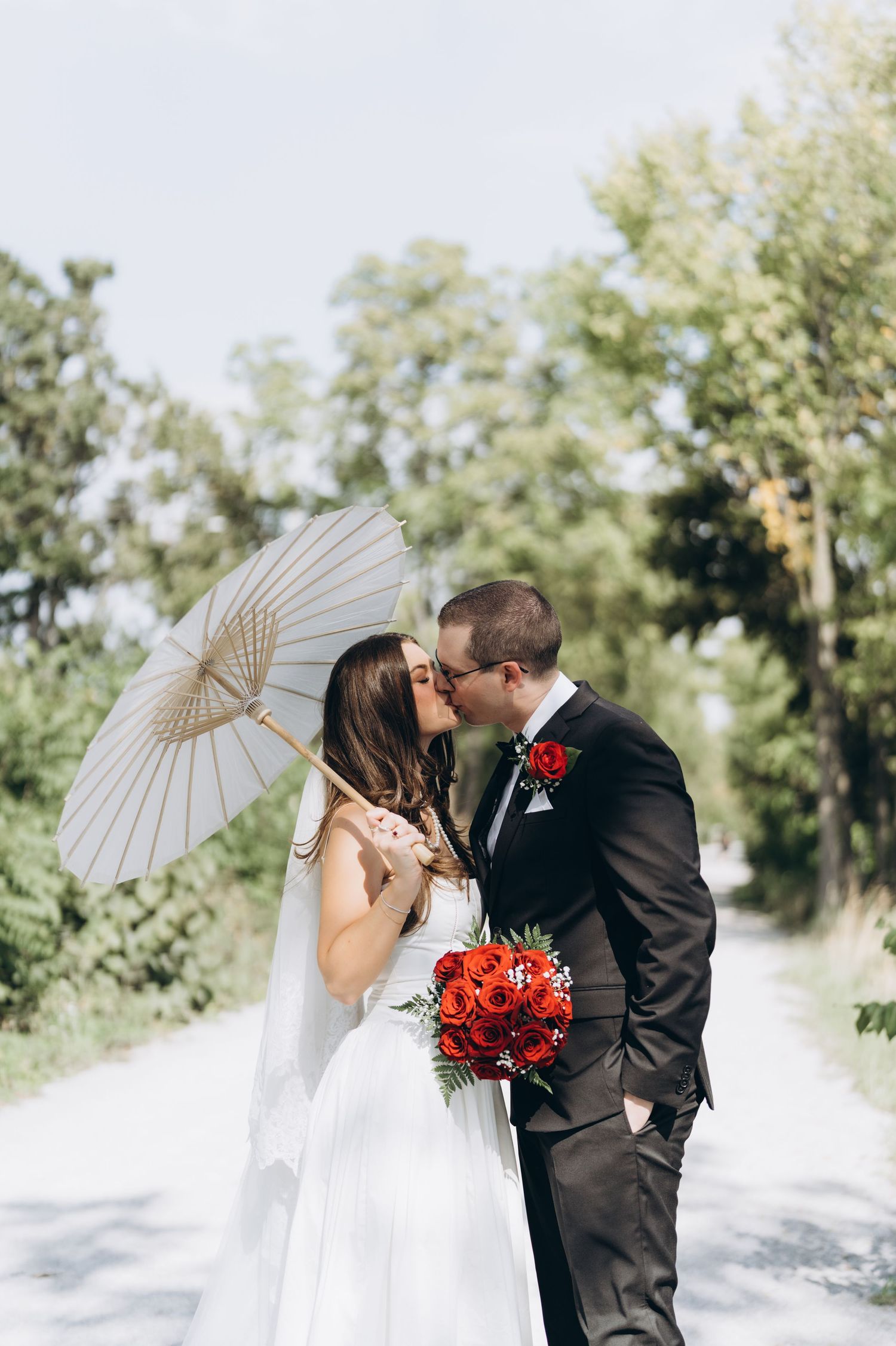 A couple poses romantically with a white parasol against a scenic outdoor background during their wedding photoshoot.