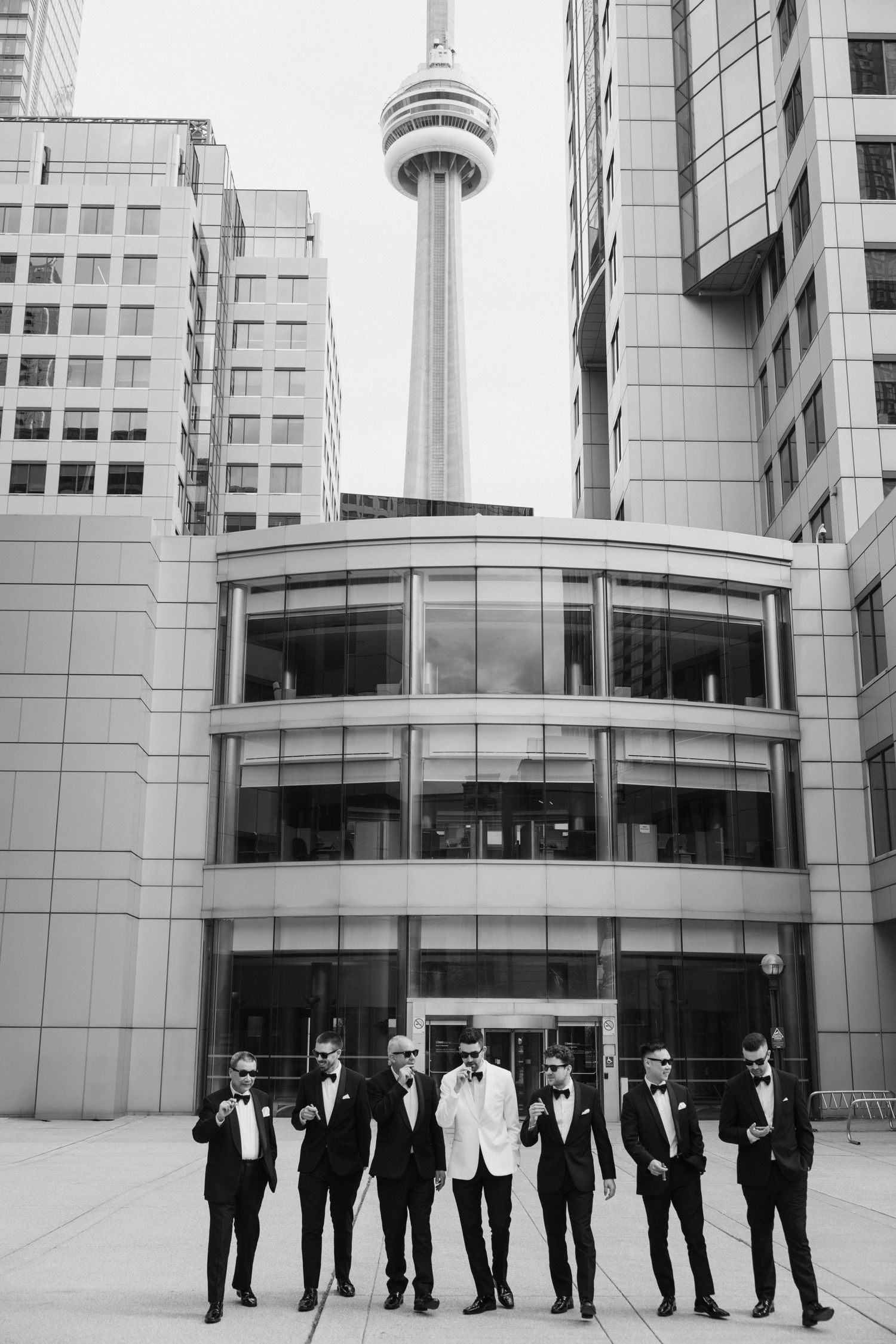 Black and white photo of a line of formally dressed wedding party members standing against a modern building facade.
