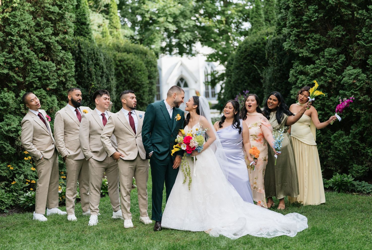 Wedding party poses together on a lush green lawn during an outdoor summer celebration.