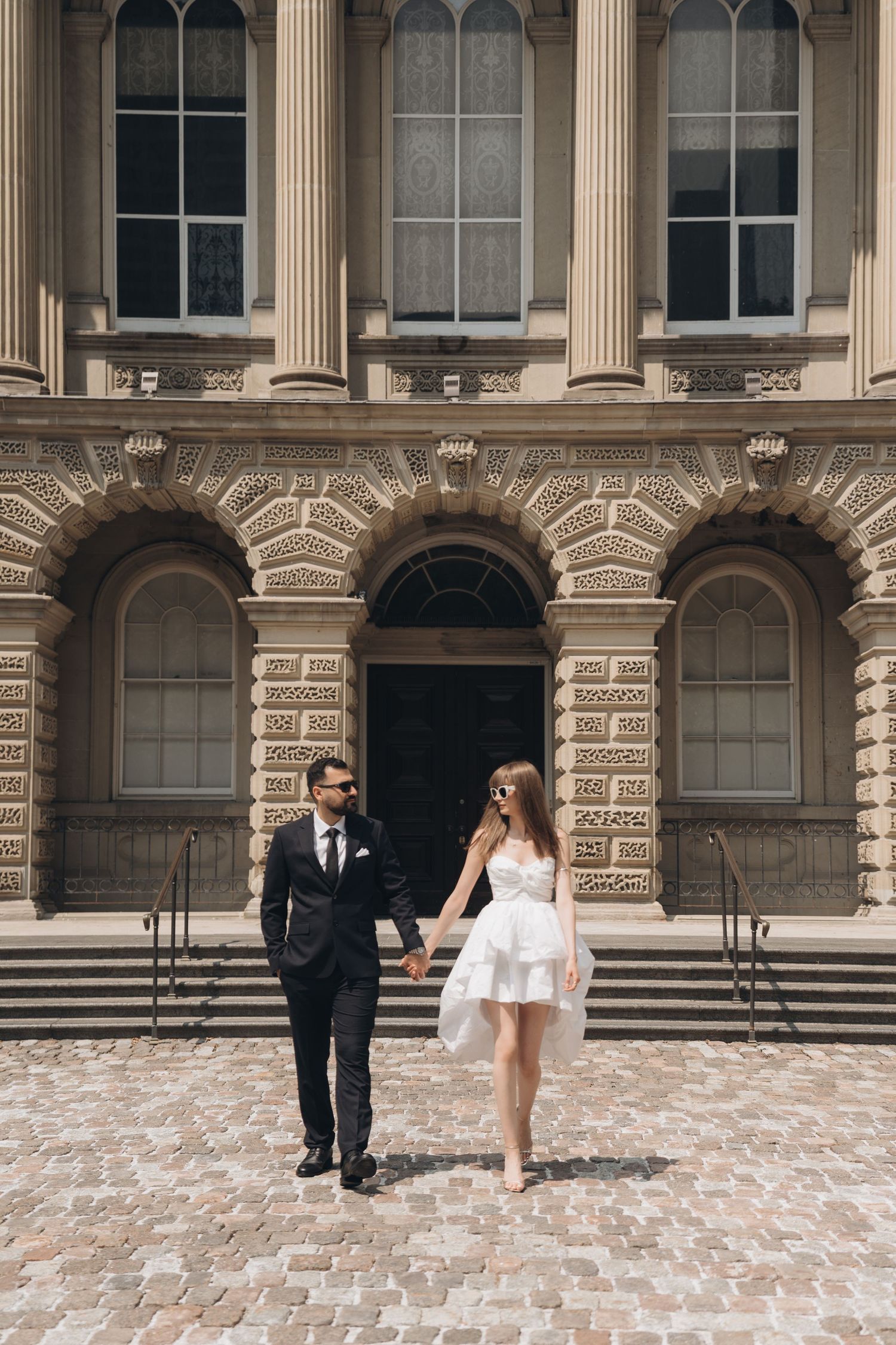 A couple's wedding photoshoot shows them walking and interacting across an elegant stone building's exterior.