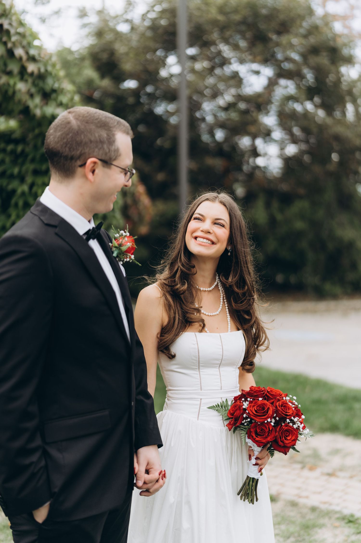 Newlywed couple shares romantic moments in outdoor photo series featuring a stunning white dress and red rose bouquet.