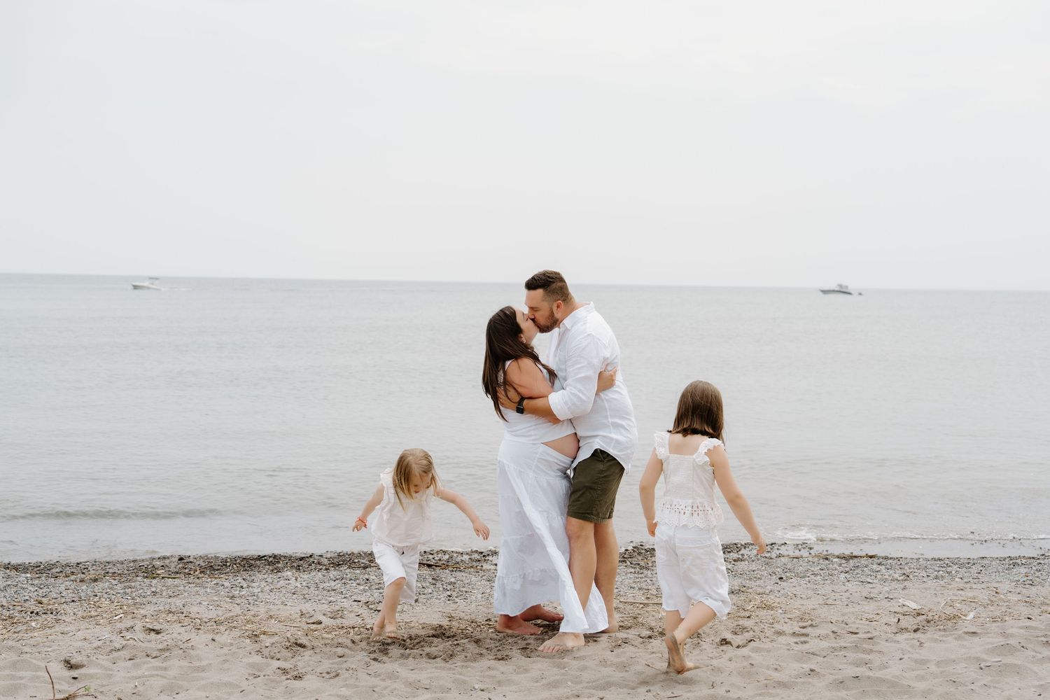 A family plays and bonds together on a sandy beach during a cloudy day by the ocean.