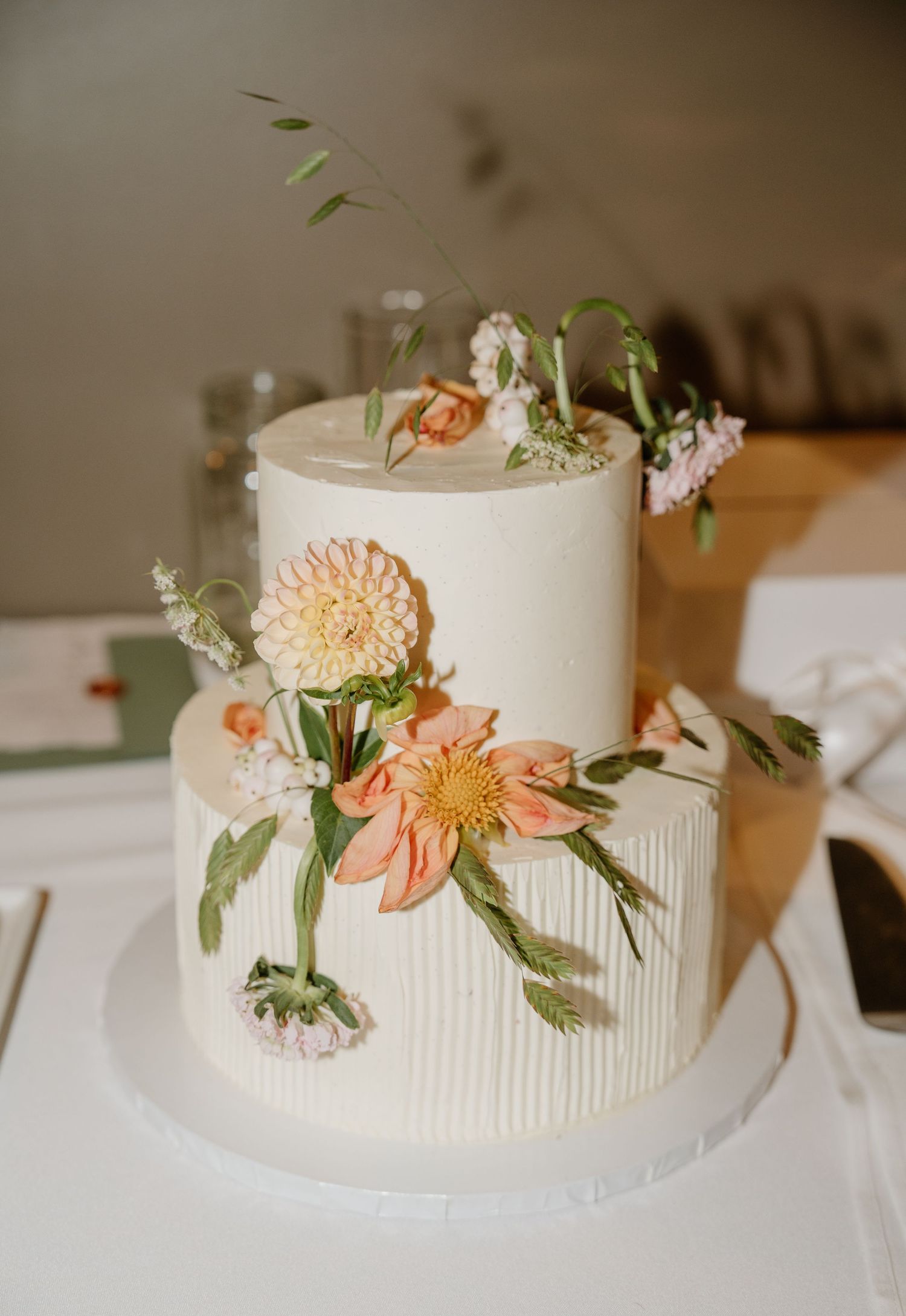 Two-tier white wedding cake decorated with peach and cream flowers and greenery.