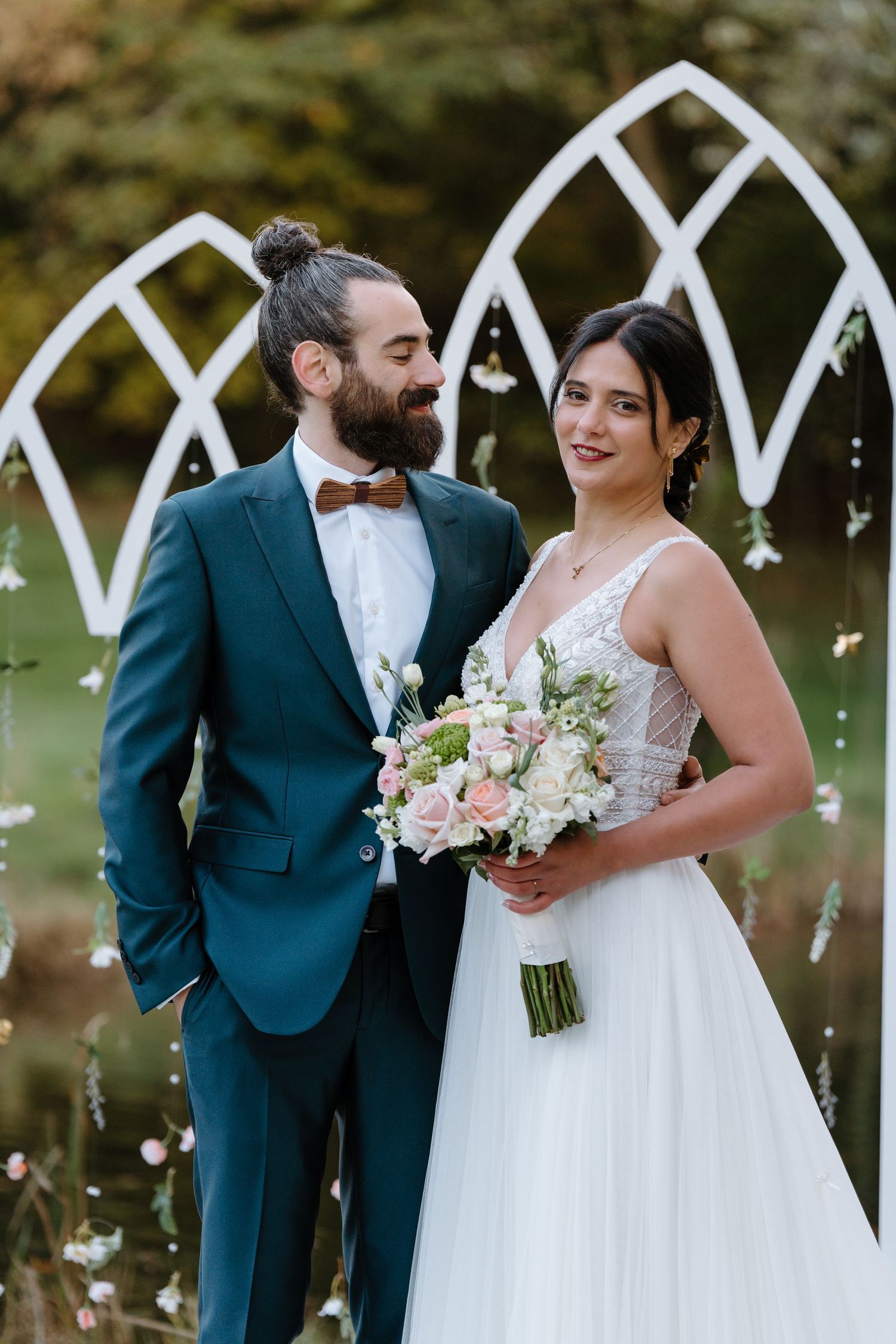 Bride and groom pose together under decorative white arches with soft lighting and floral details.