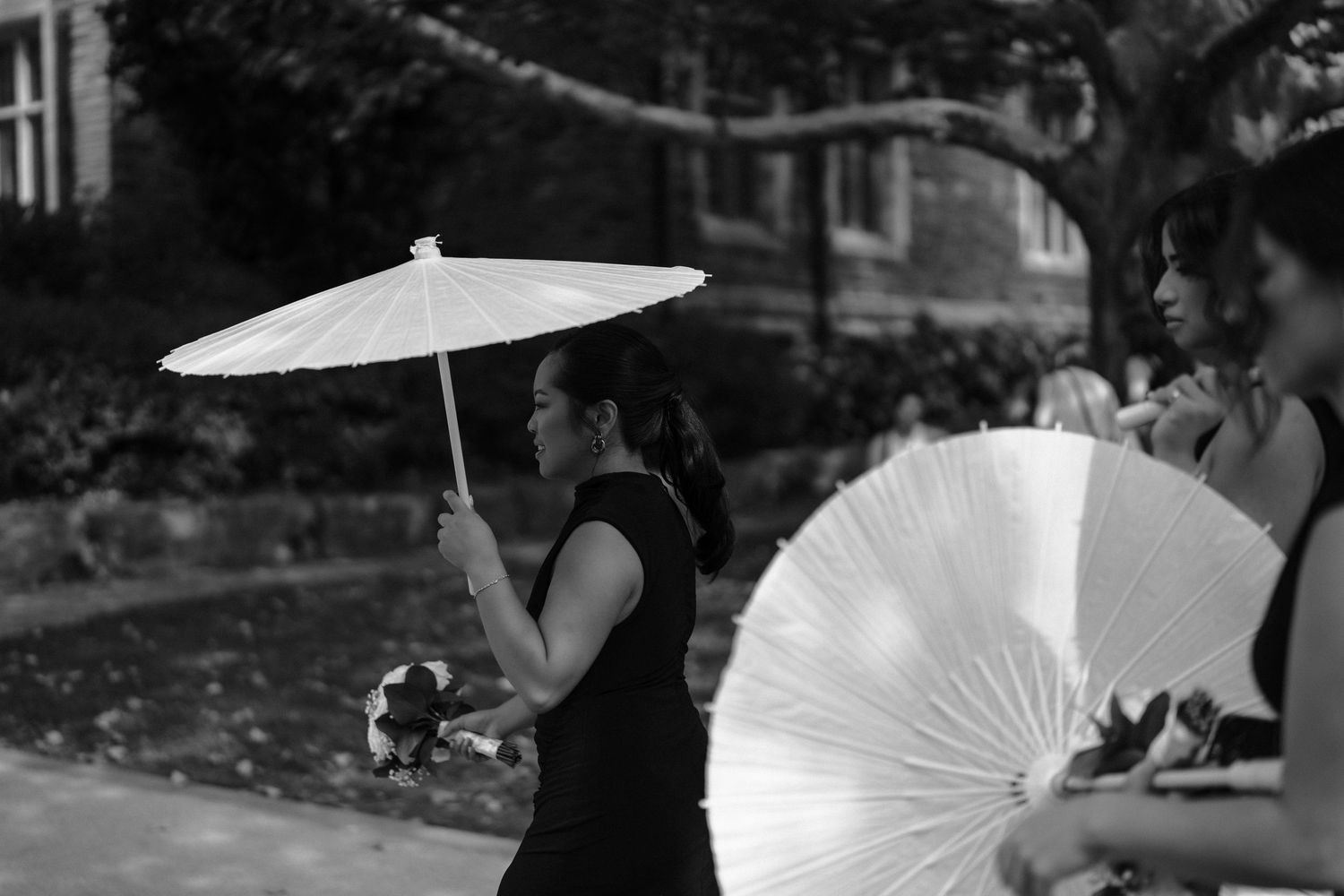 Wedding party members holding white parasols during an outdoor summer ceremony in black and white.