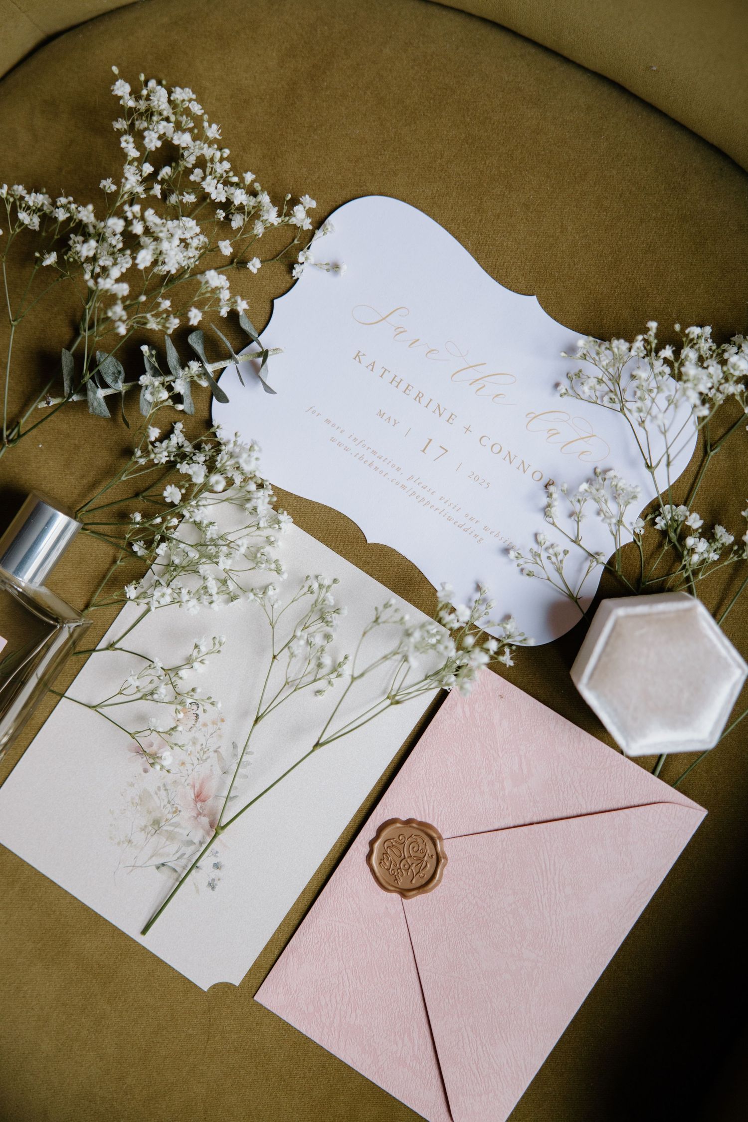 Elegant wedding stationery with white invitation cards, pink envelope with wax seal, and delicate baby's breath flowers arranged.