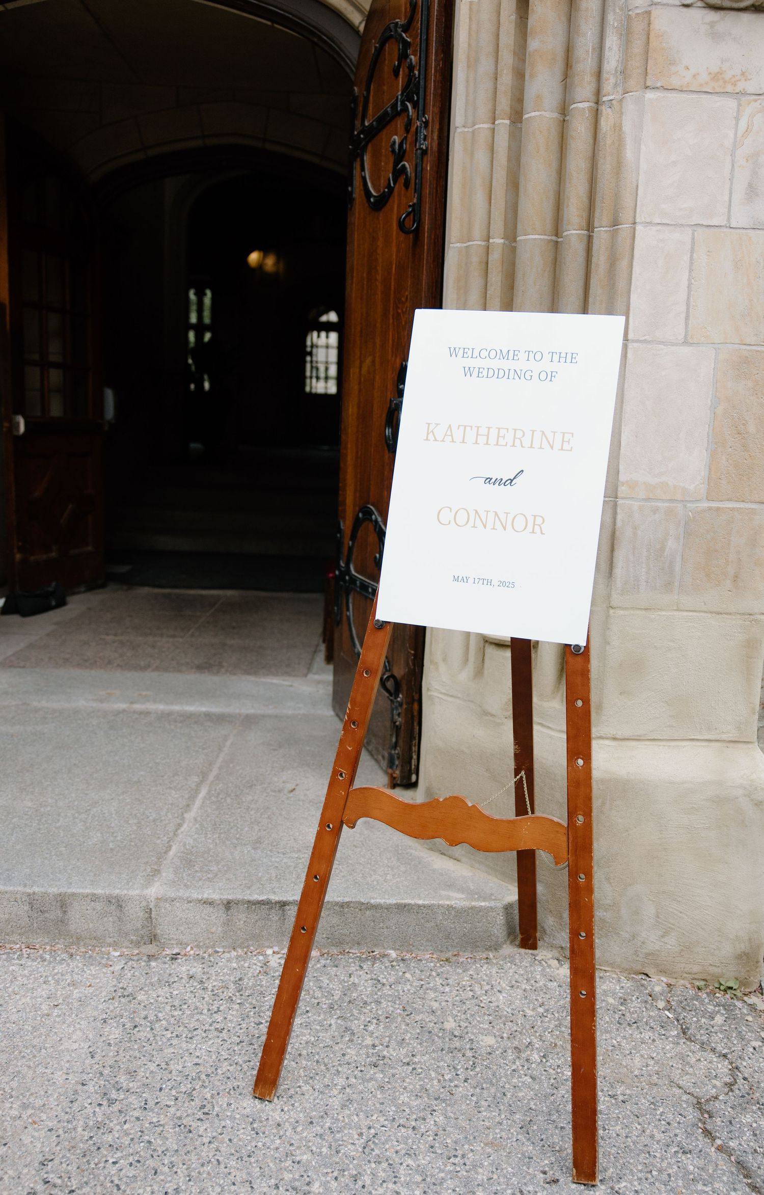 A wooden easel with a white paper sign stands at the entrance of a stone archway with a wooden door.