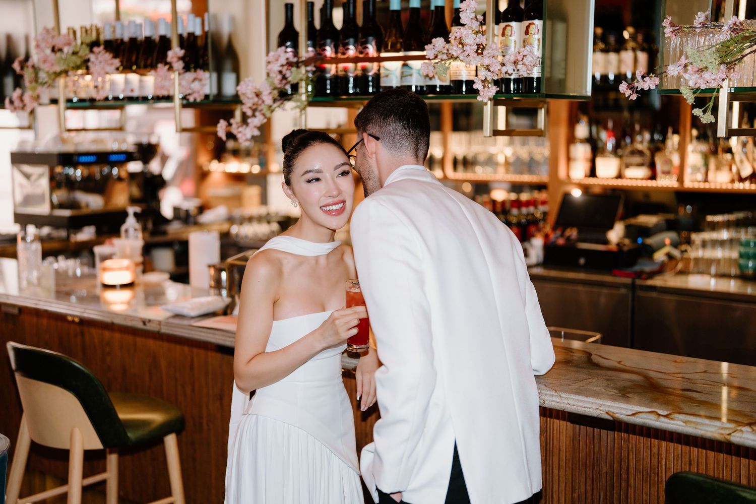 A couple in wedding attire dances together lovingly in an intimate restaurant setting with a wooden bar in the background.