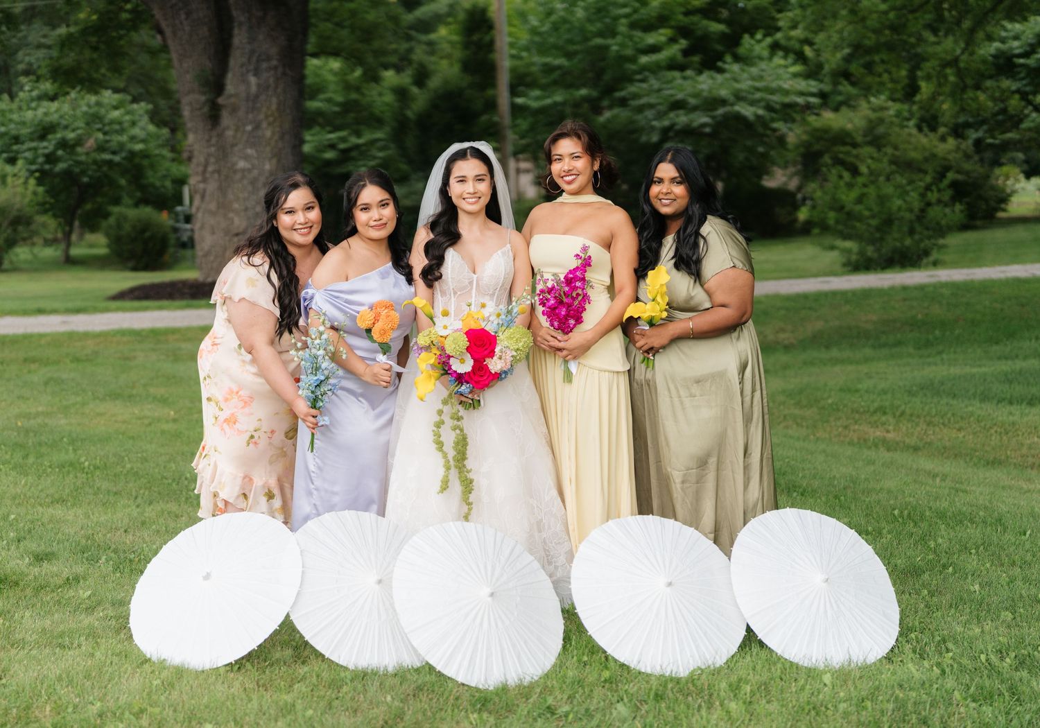 A group in formal attire poses outdoors with decorative white parasols in a garden setting.