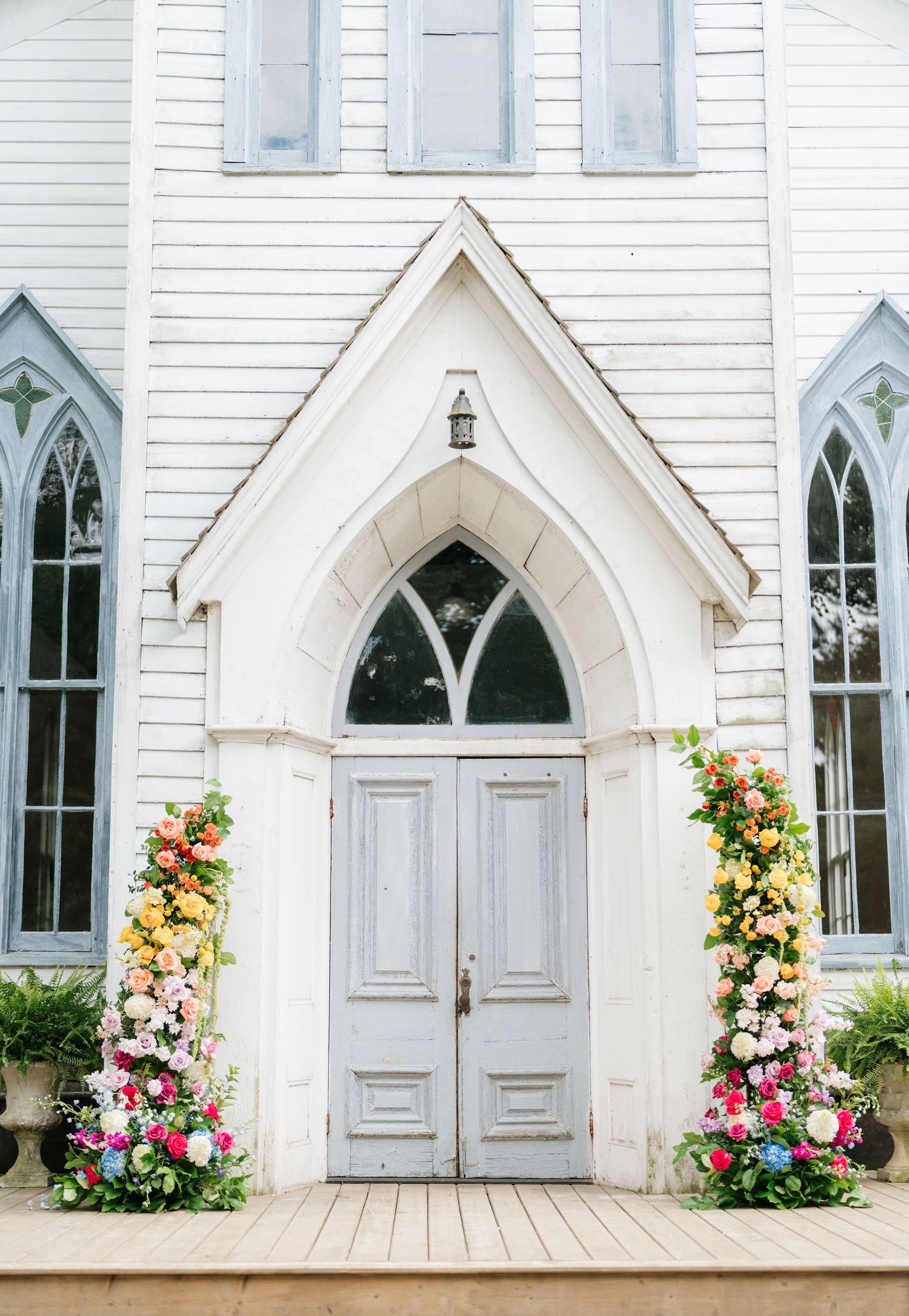 White gothic church windows and doors decorated with colorful floral arrangements in pink, yellow and orange blooms.
