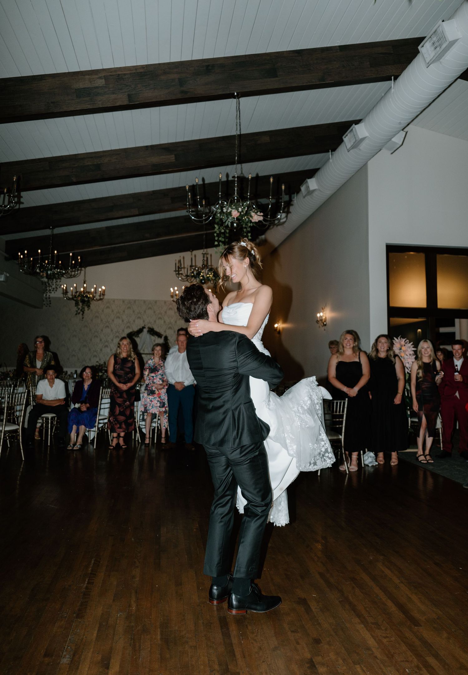 Couples dancing at a wedding reception in an elegant venue with dark hardwood floors and chandeliers.
