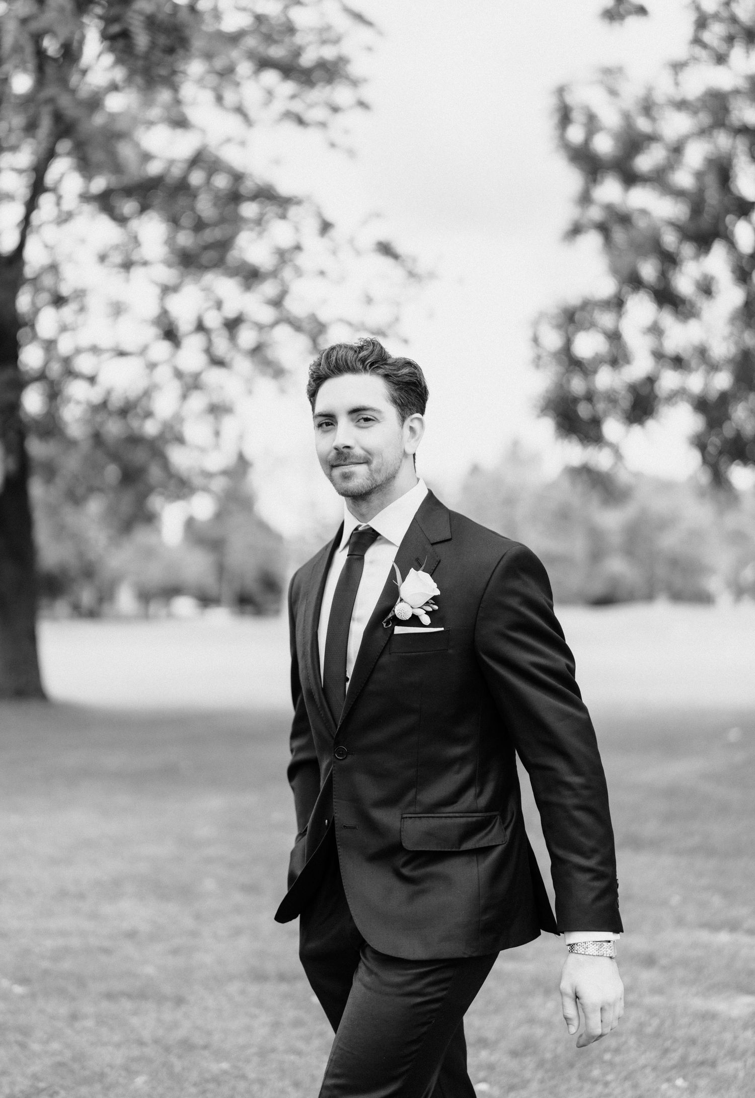 Black and white portrait of groom in formal attire walking outdoors.